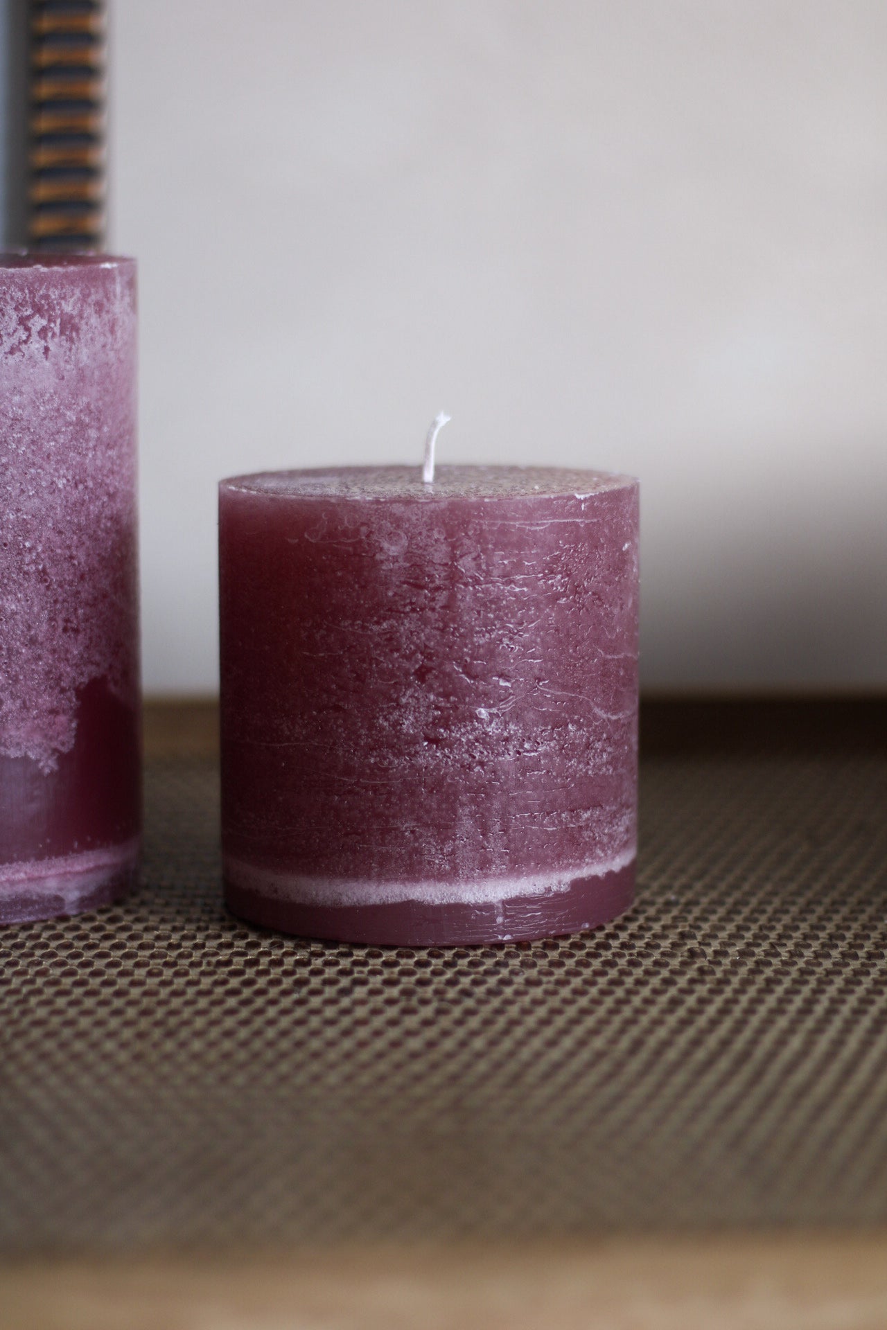Two plum candles on a textured surface with a neutral background