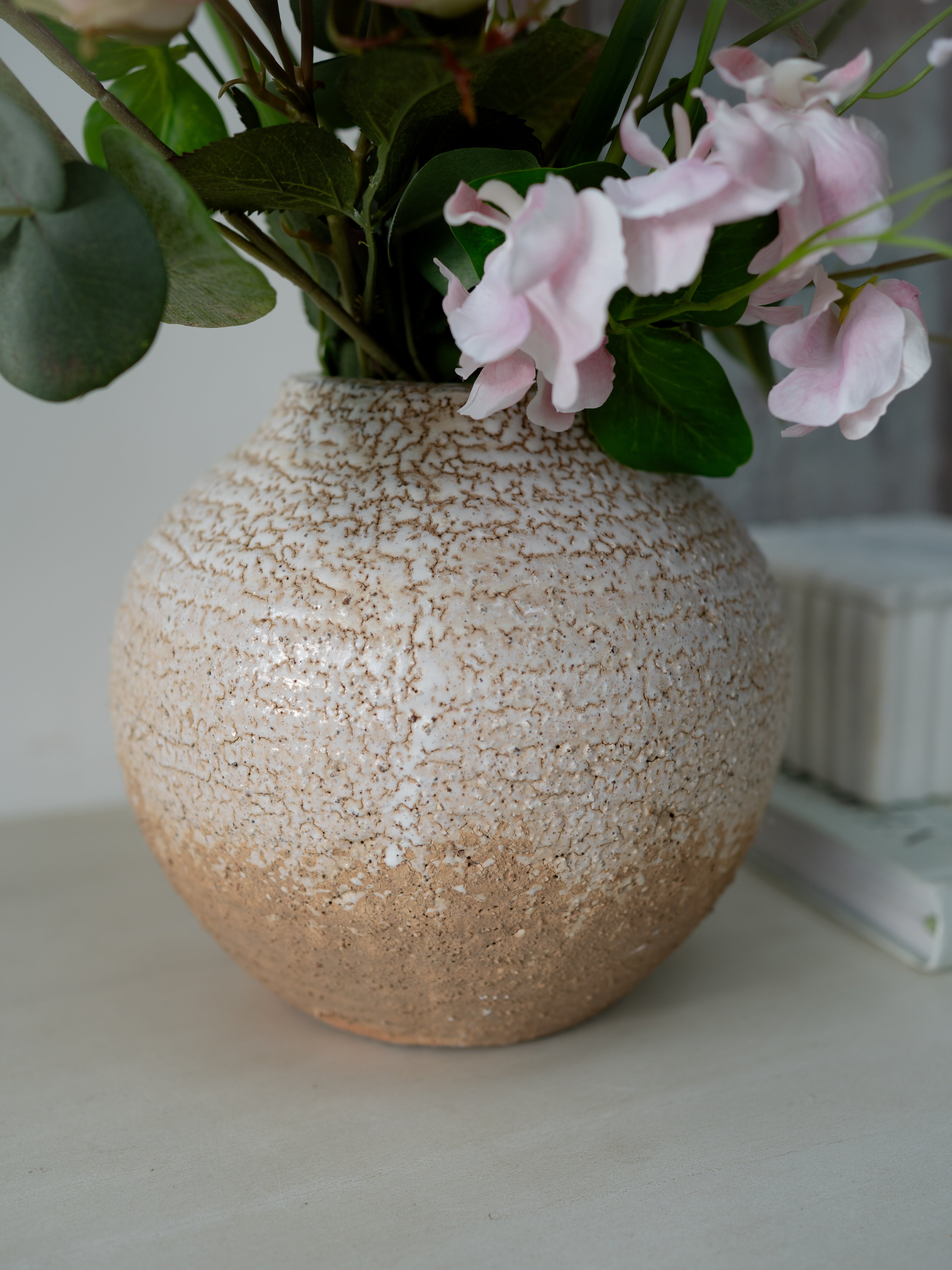 Textured ceramic vase with pink flowers and green leaves on a light surface.