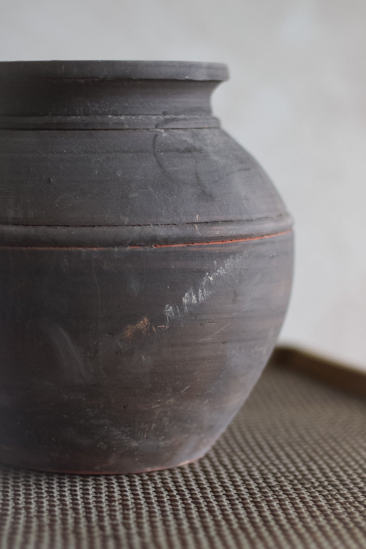 Earth brown ceramic jar on a textured surface with a neutral background