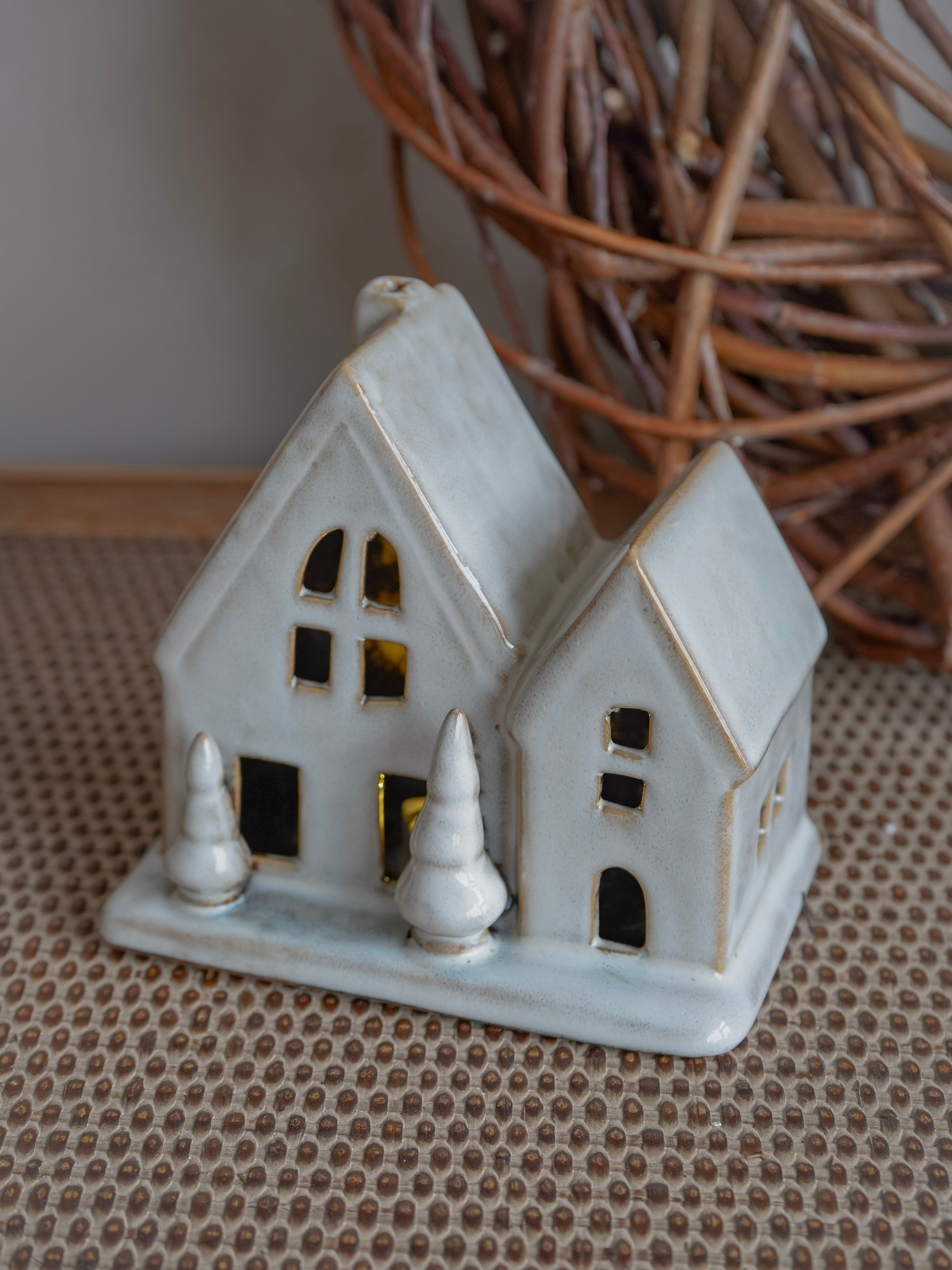 Small ceramic house ornament on a textured surface with a wicker basket in the background.