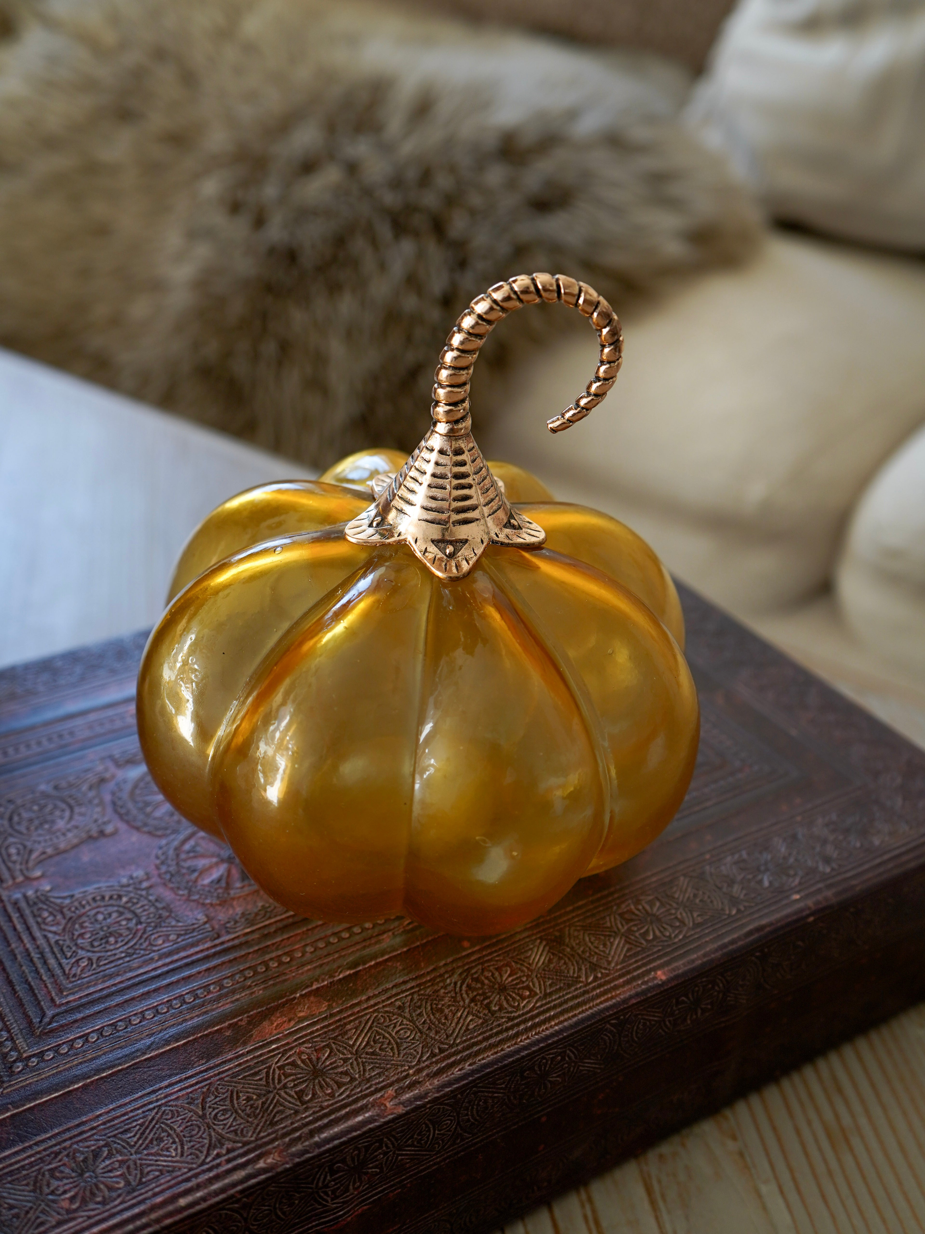 Decorative amber glass pumpkin with a textured surface on a wooden table.