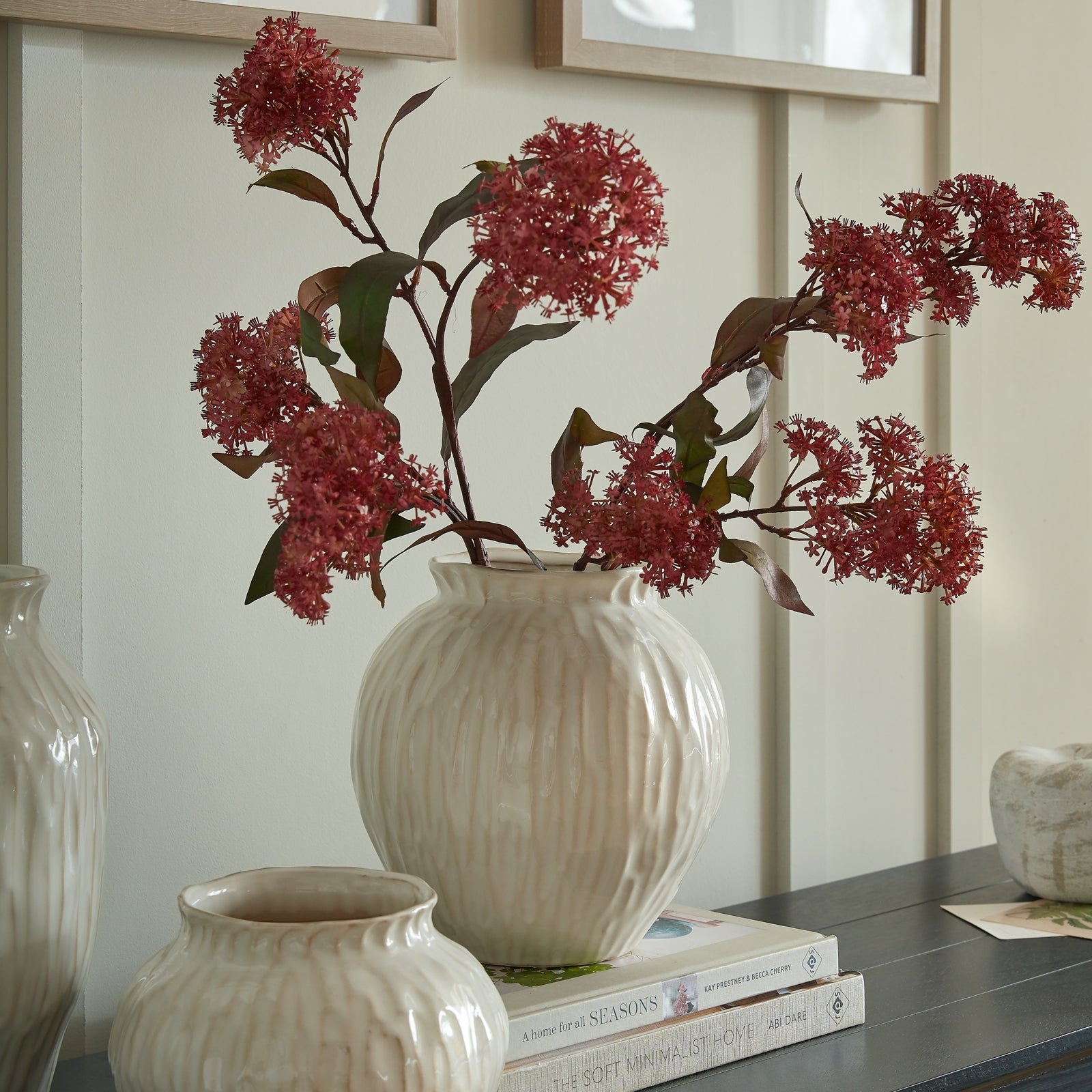 Decorative arrangement with red flowers in a white vase on a shelf.