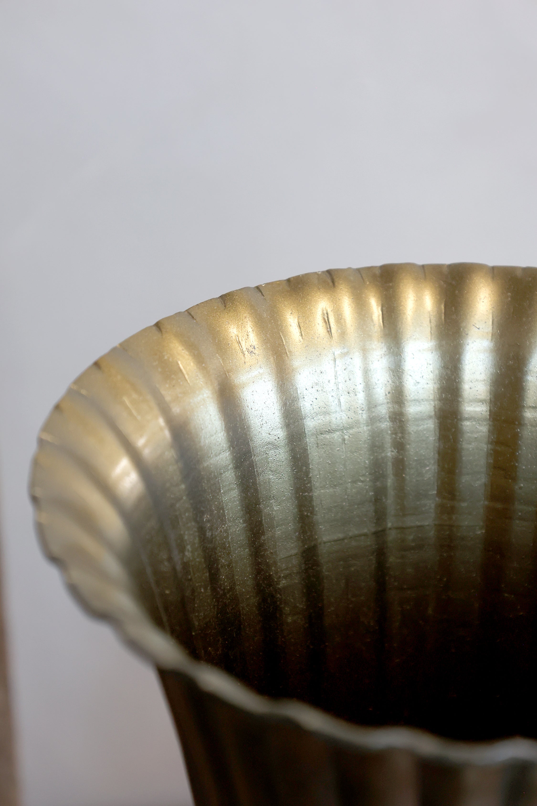 Close-up of a metallic fluted cup or vase rim with a brushed gold and silver finish against a plain light background.