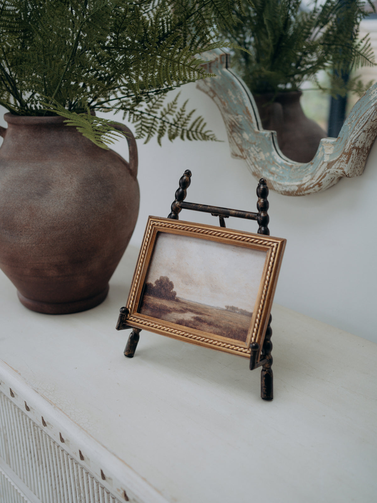 Antique Gold Beaded Mini Easel with vintage style landscape artwork and terracotta amphora style vase with faux ferns in the background