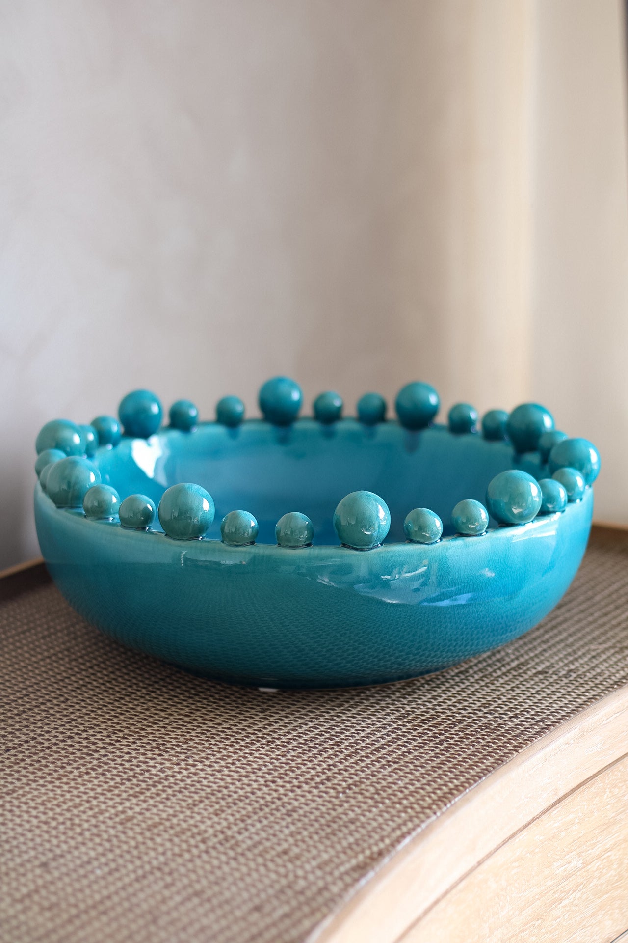 aqua ceramic bowl with bobble-like embellishments on a textured surface.