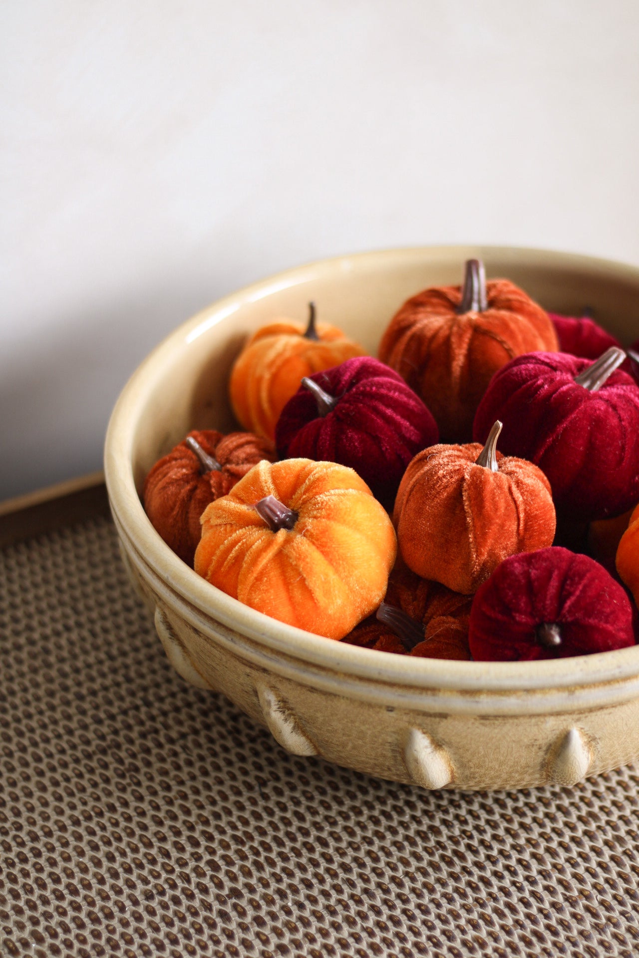 Decorative pumpkins in a ceramic bowl on a textured surface