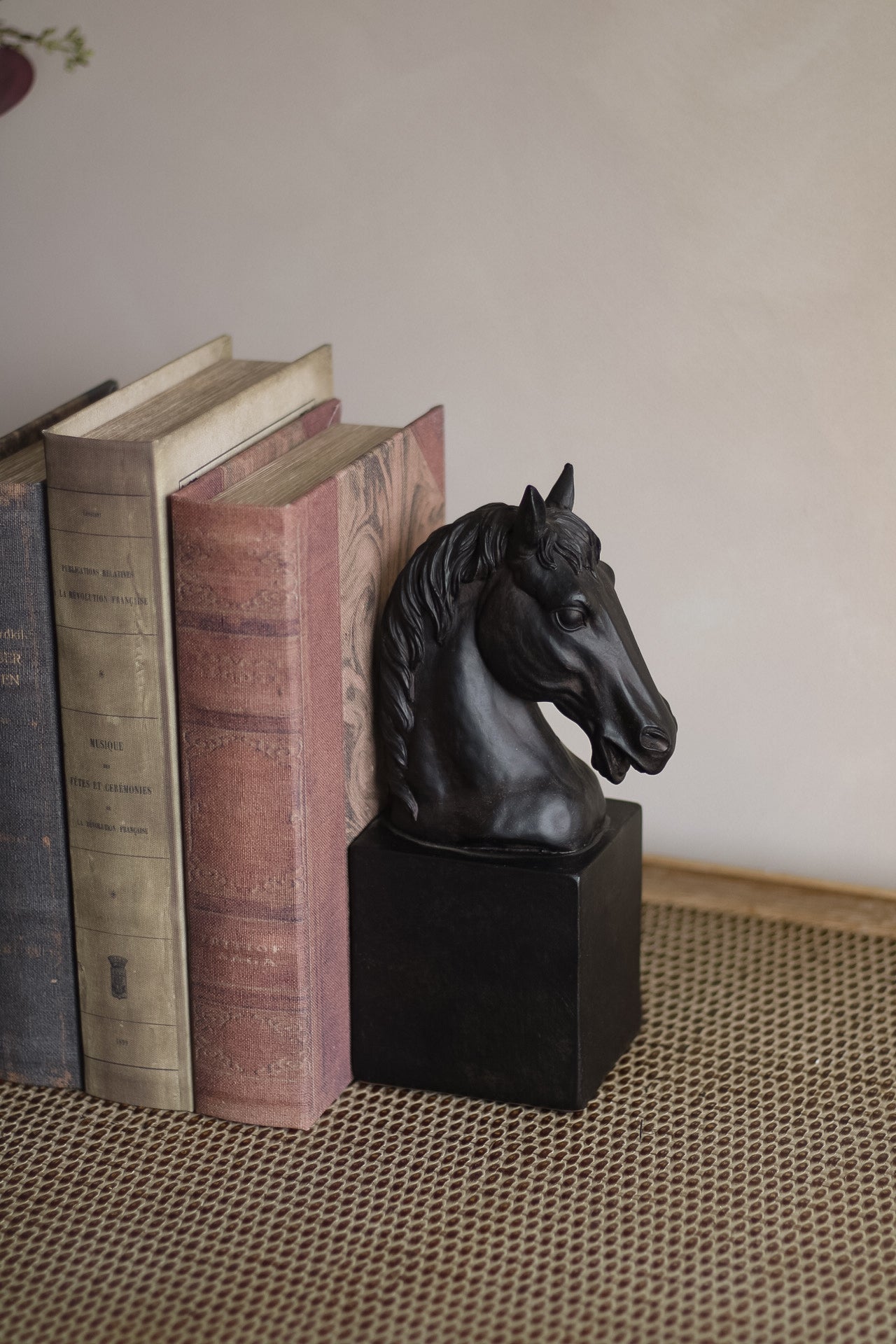 Horse head bookend on a stack of books with a neutral background