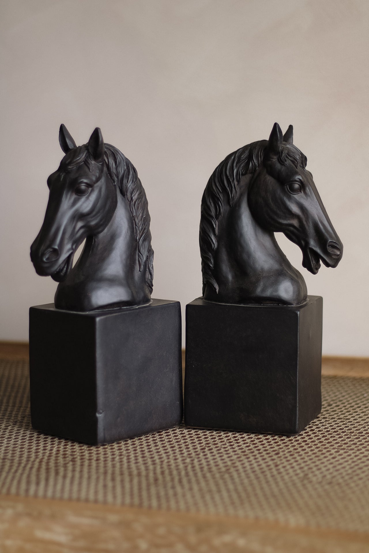 Two black horse head sculptures on hexagonal bases against a neutral background