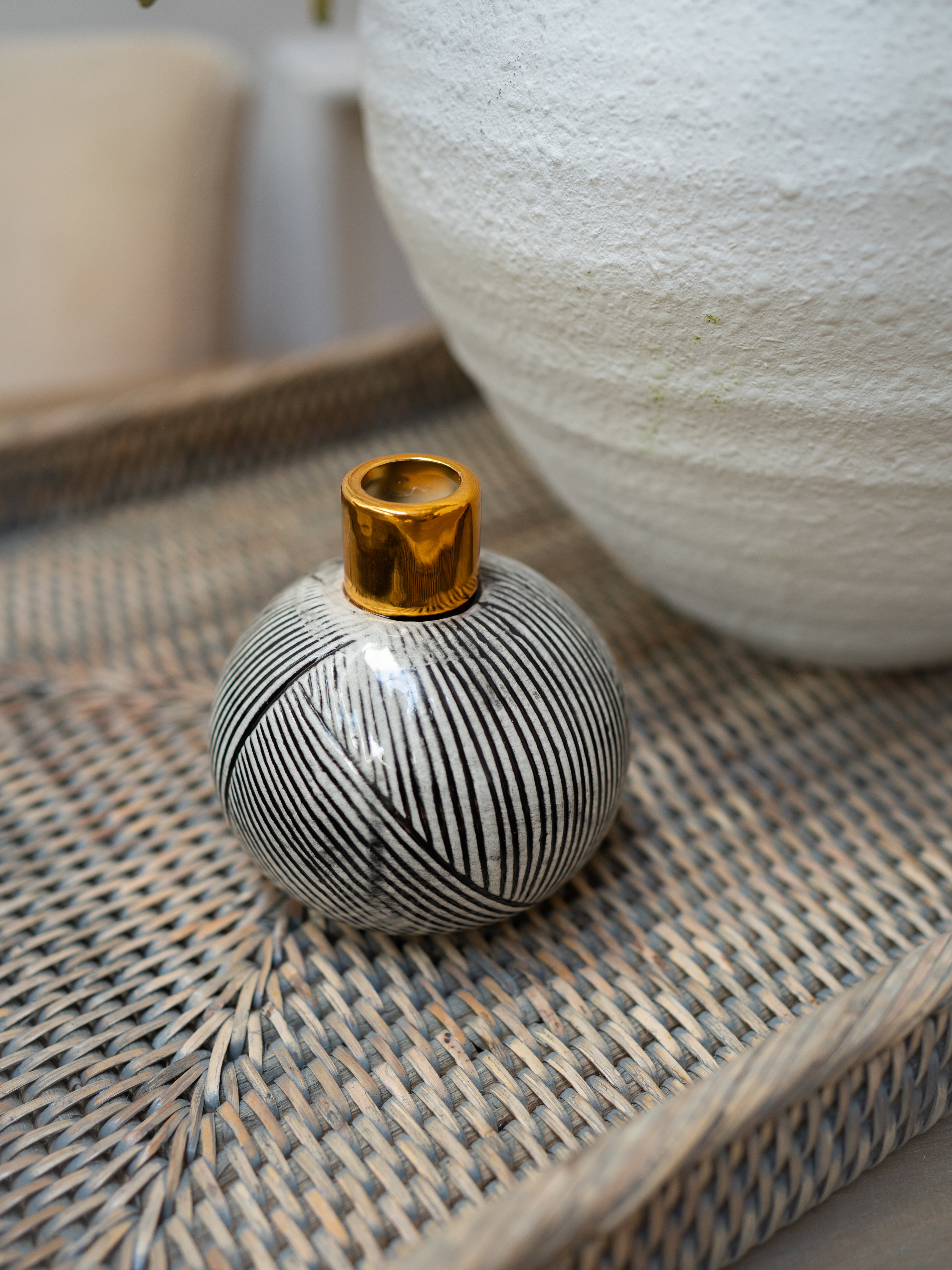 Small black and white striped vase with gold top on a textured surface