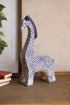 Decorative giraffe figurine with blue and white pattern on a beige wall and textured floor.