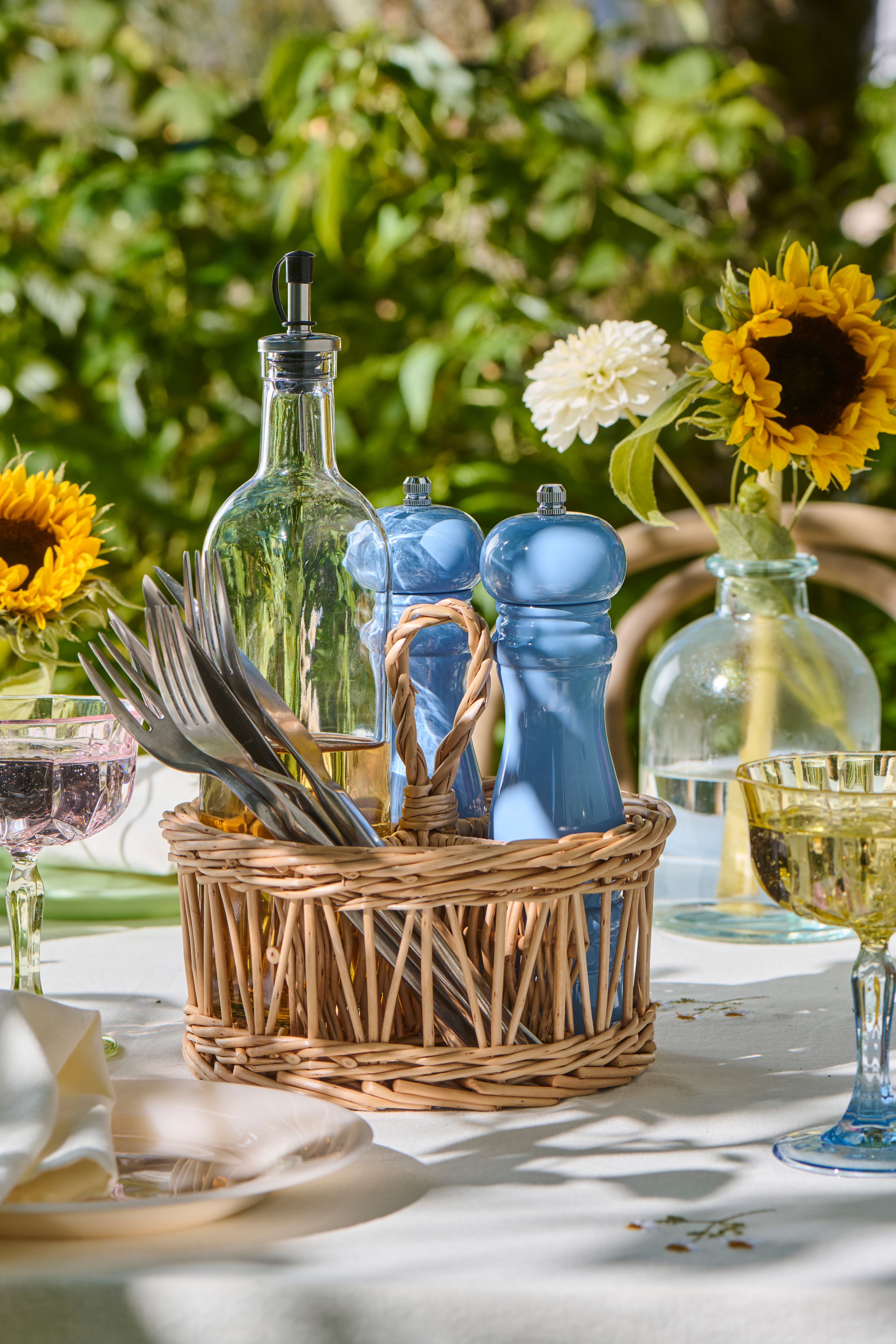 Table setting with a basket of cutlery, glass bottles, and flowers outdoors.