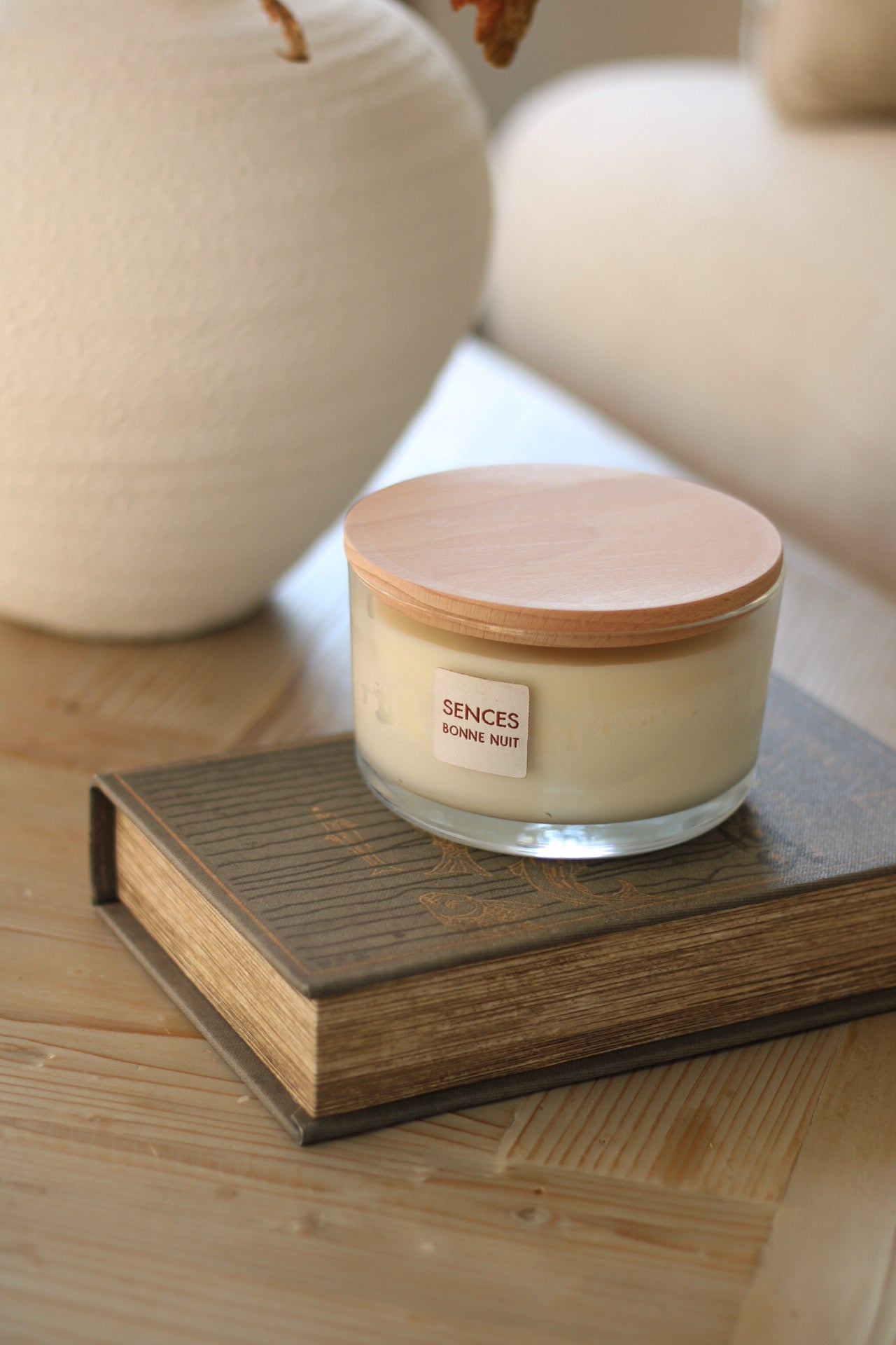 Sences candle in Bonne nuit lavender scent with wooden lid on a book, surrounded by decorative items