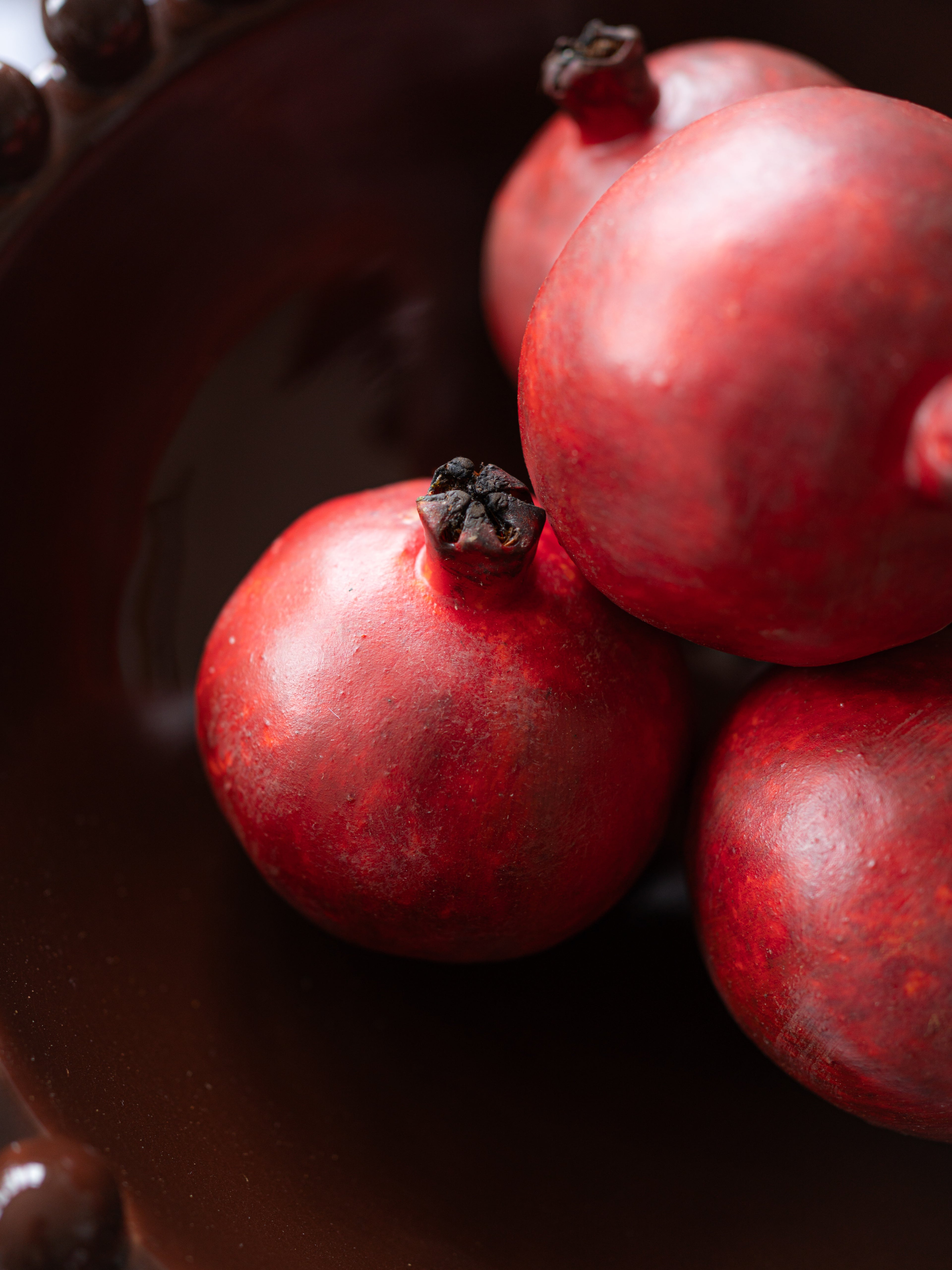 Several faux red pomegranates clustered together in a dark, close-up still life.