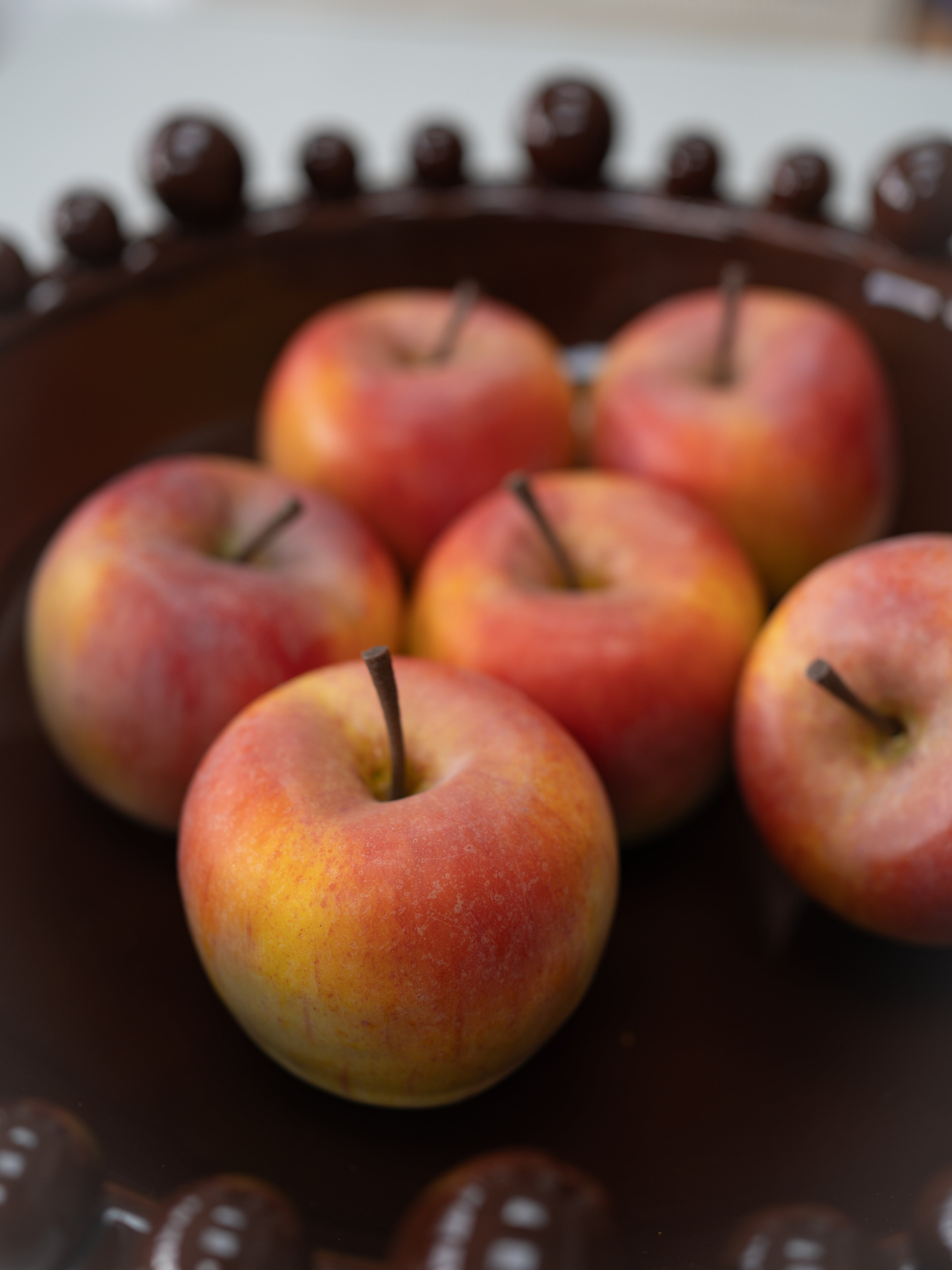Several red and yellow apples arranged on a dark brown decorative plate with a beaded rim.
