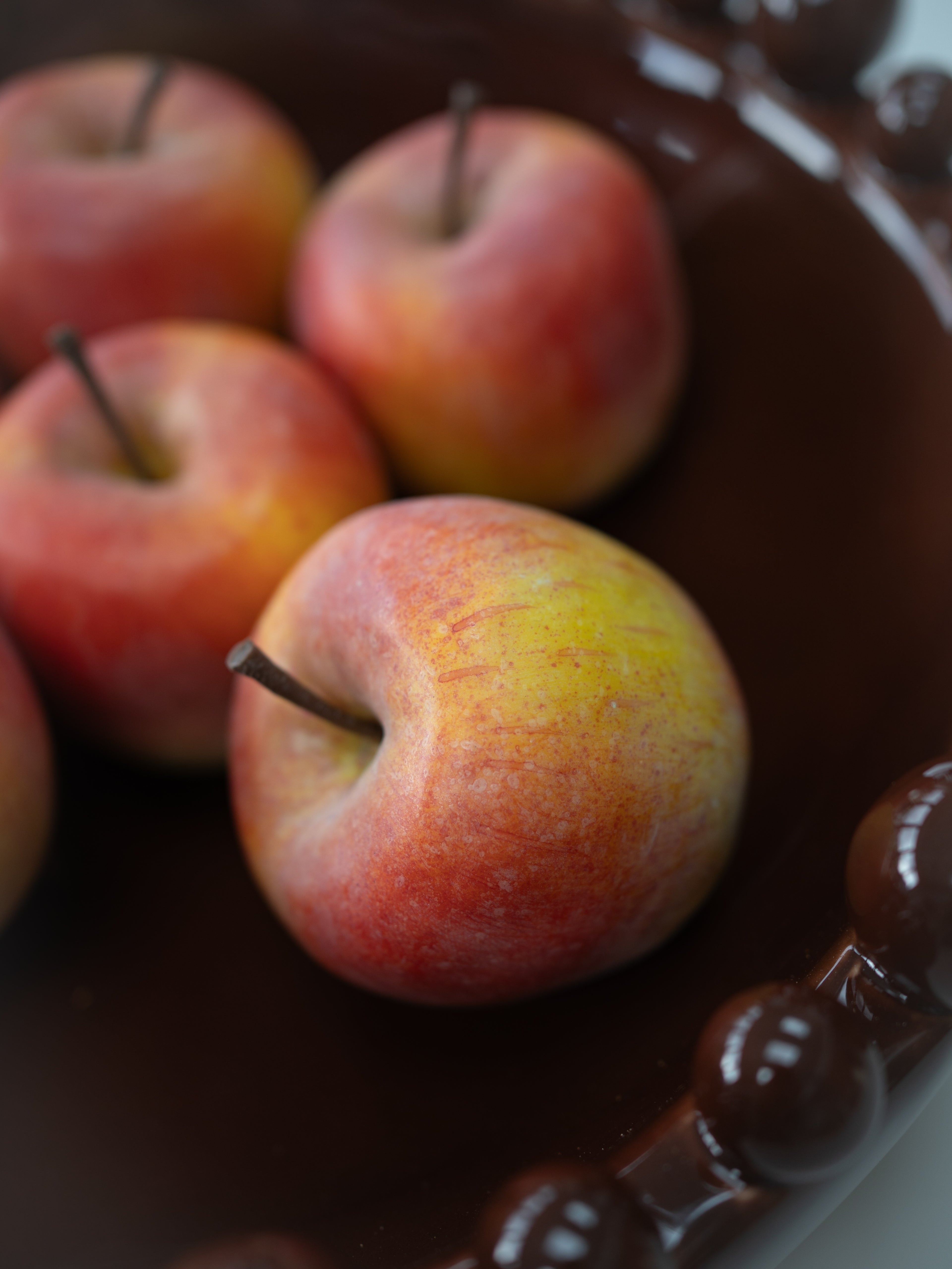 A close-up shot of several faux red and yellow apples resting in a dark brown ceramic bowl with a beaded rim.
