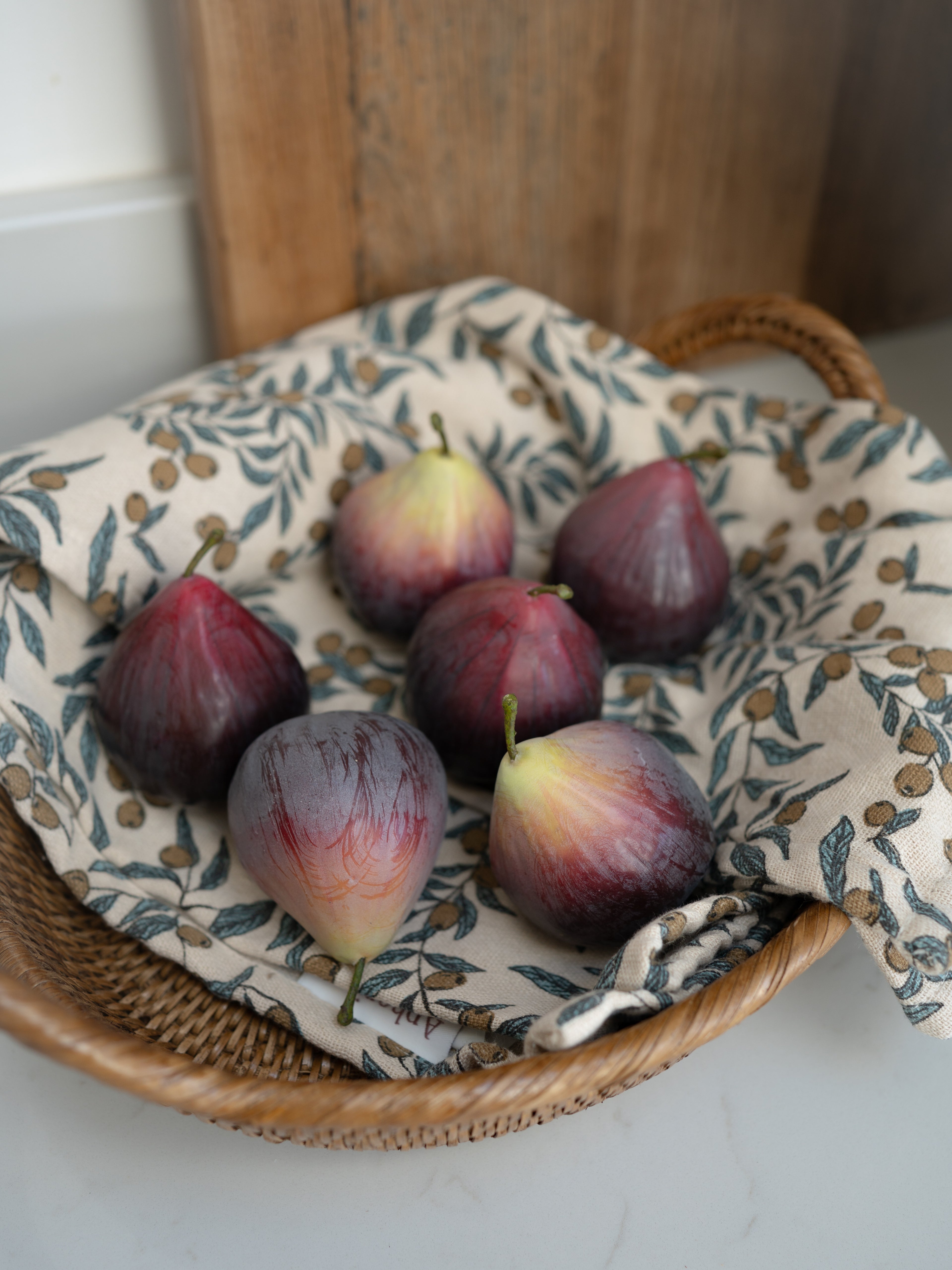Decorative faux figs on a woven basket with a patterned cloth underneath