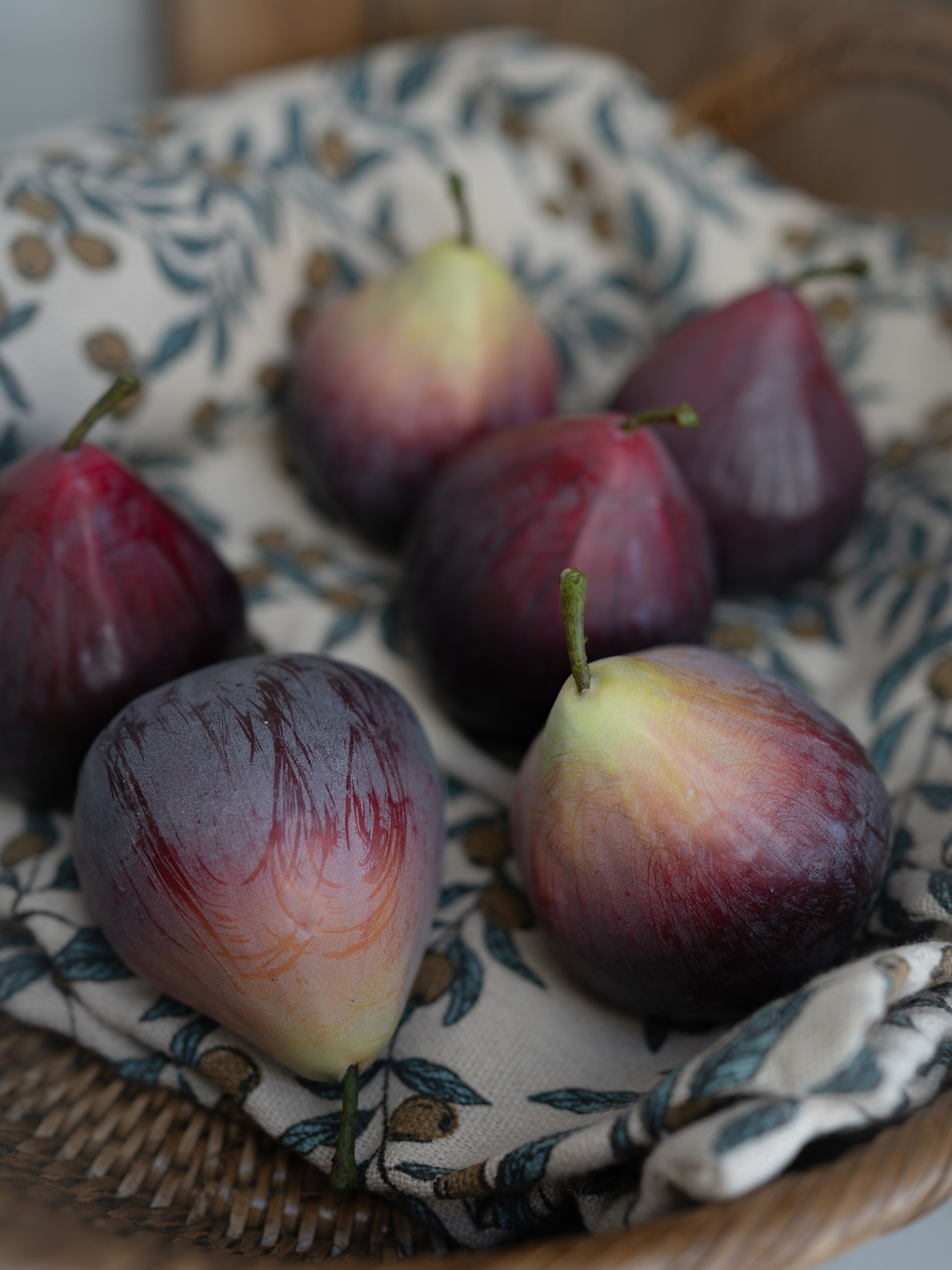 Decorative faux figs on a woven basket with a patterned cloth underneath