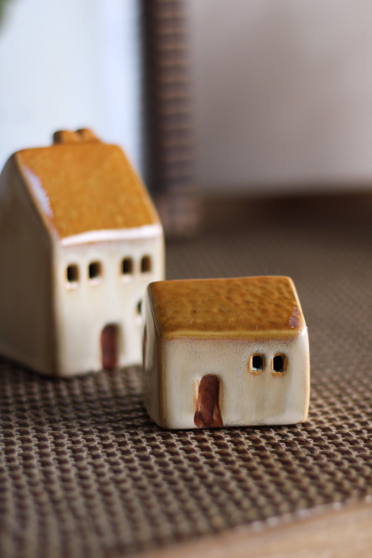 Two small ceramic houses with brown roofs on a textured surface.