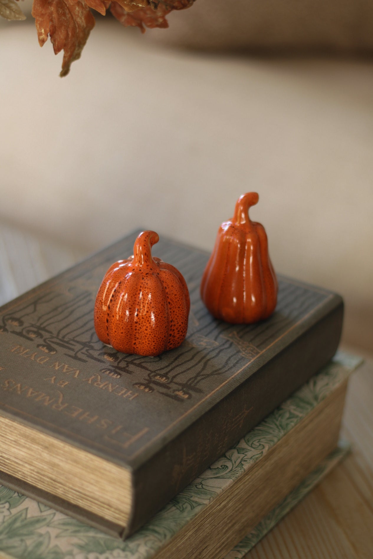 Two small orange pumpkins on a book with a neutral background