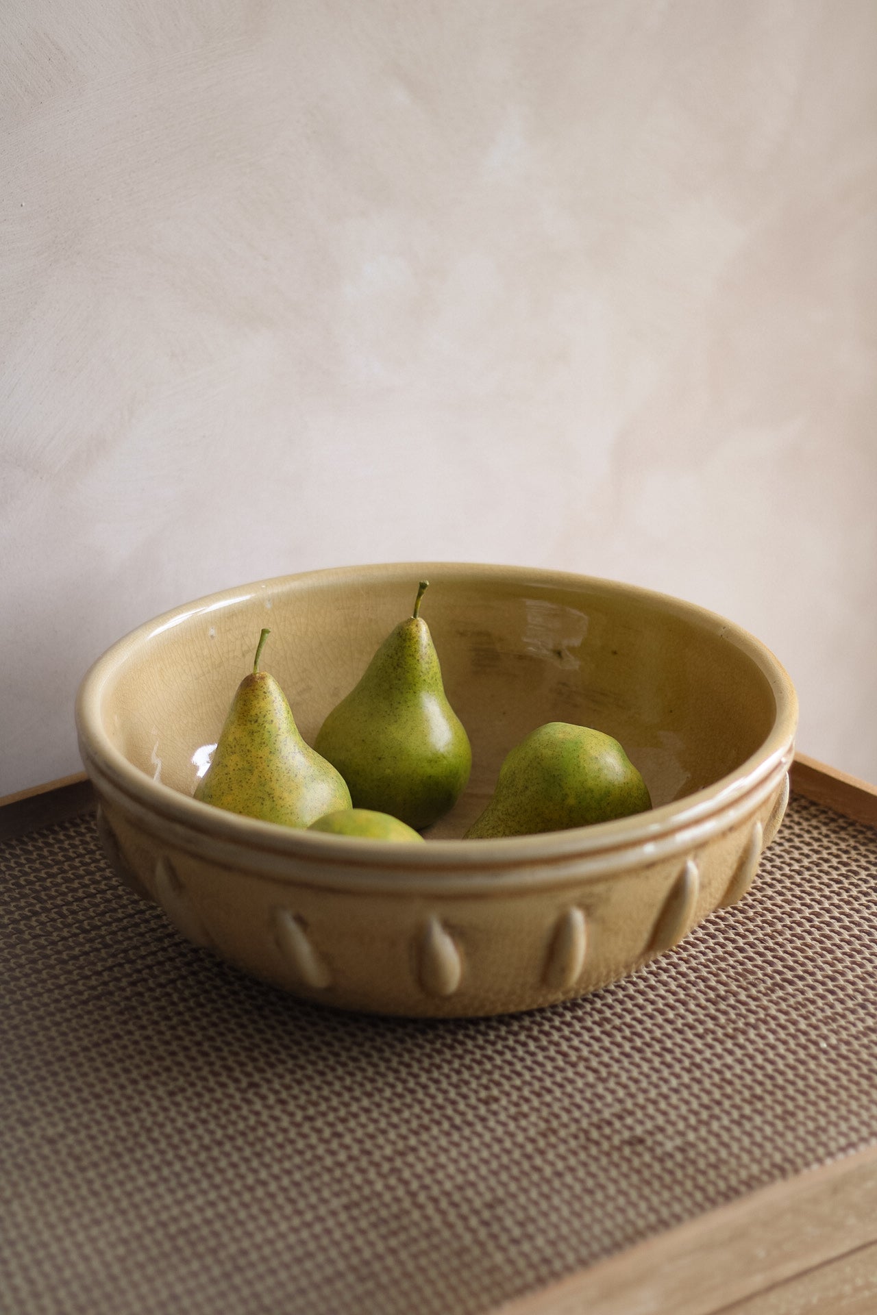 Ochre ceramic bowl with three green pears on a textured surface.