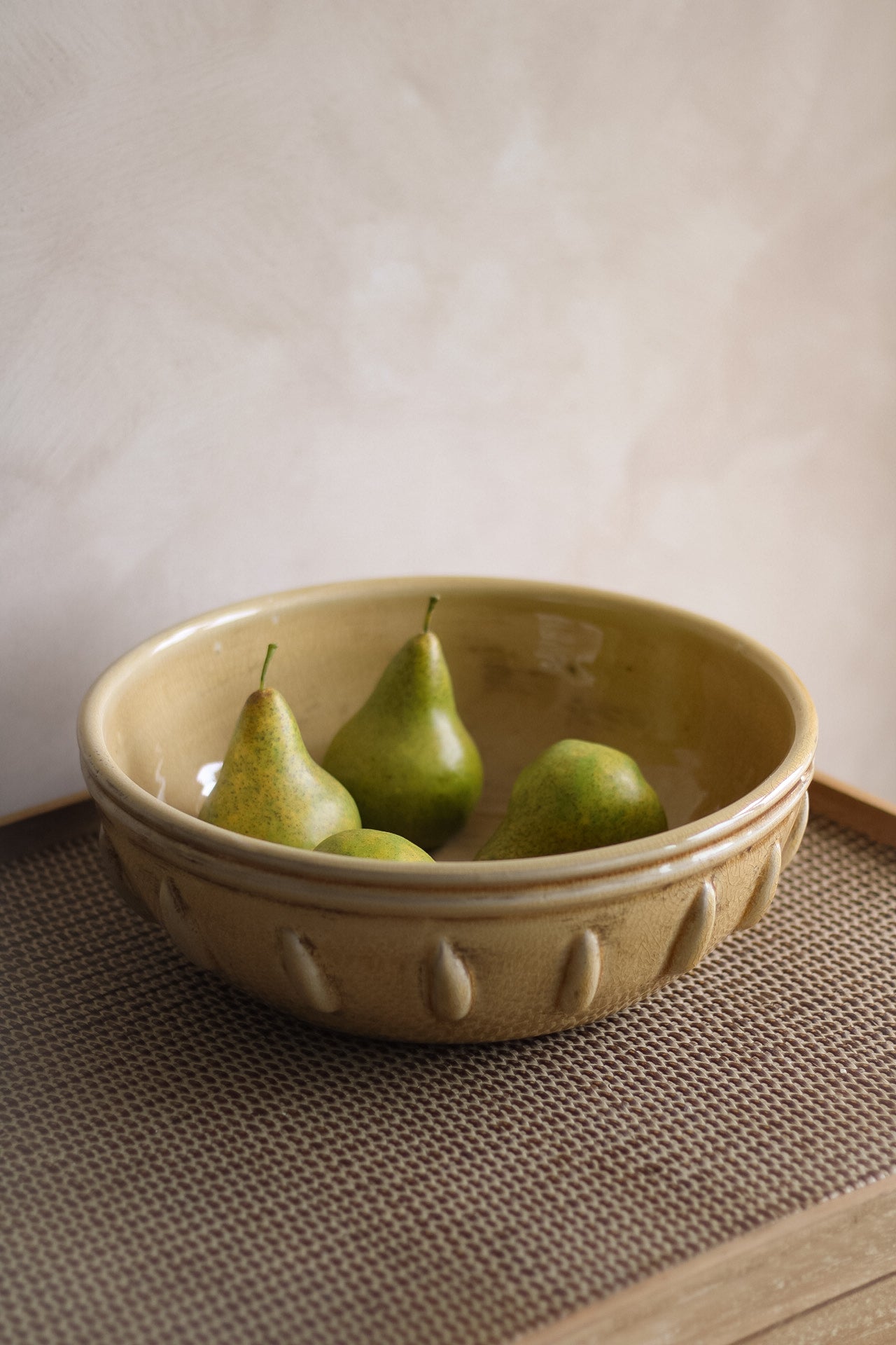 Mustard ceramic bowl with three green pears on a textured surface.