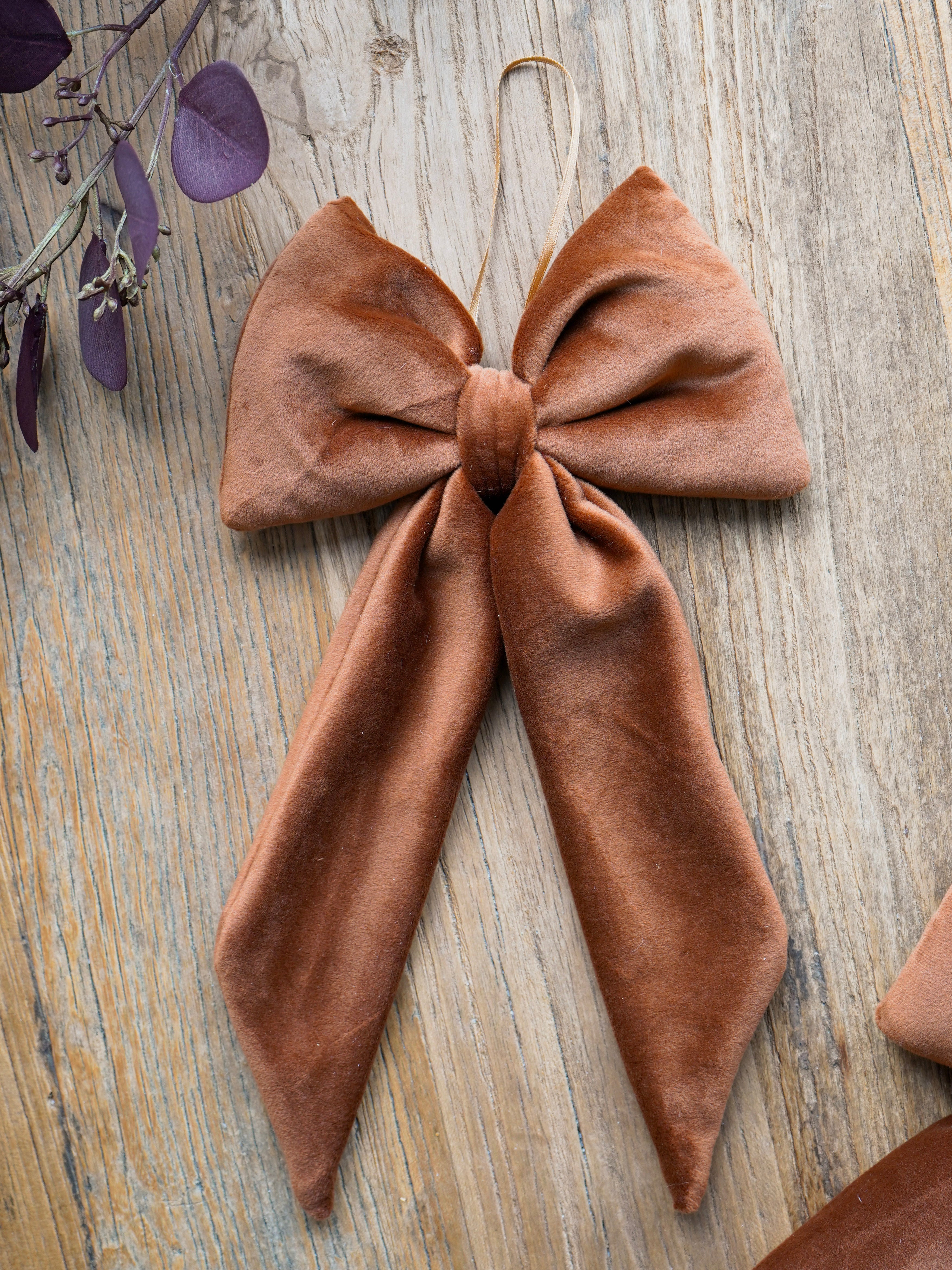 caramel bow-shaped decorative item on a wooden surface with purple leaves.