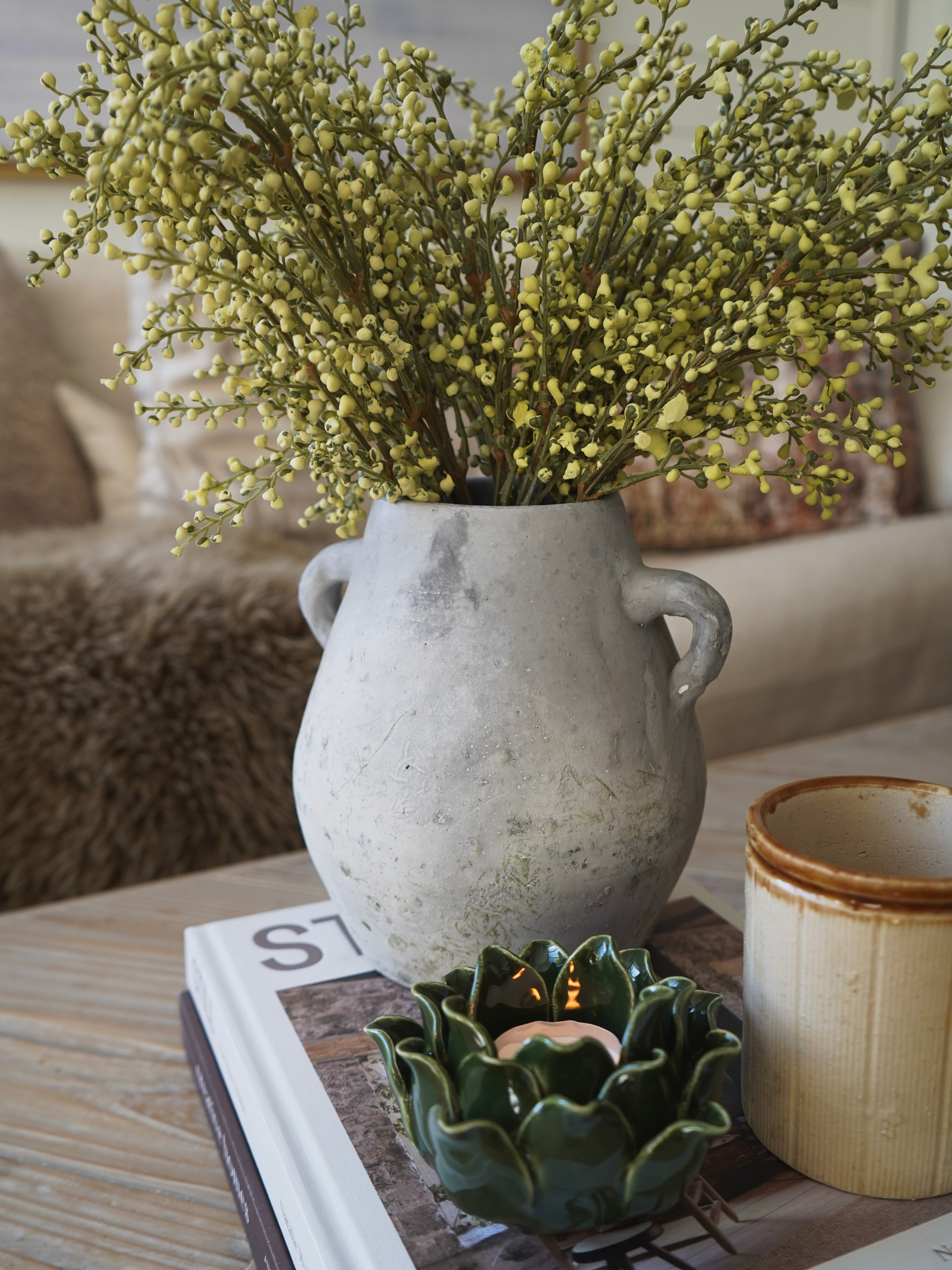Decorative vase with greenery on a coffee table with a candle and book.