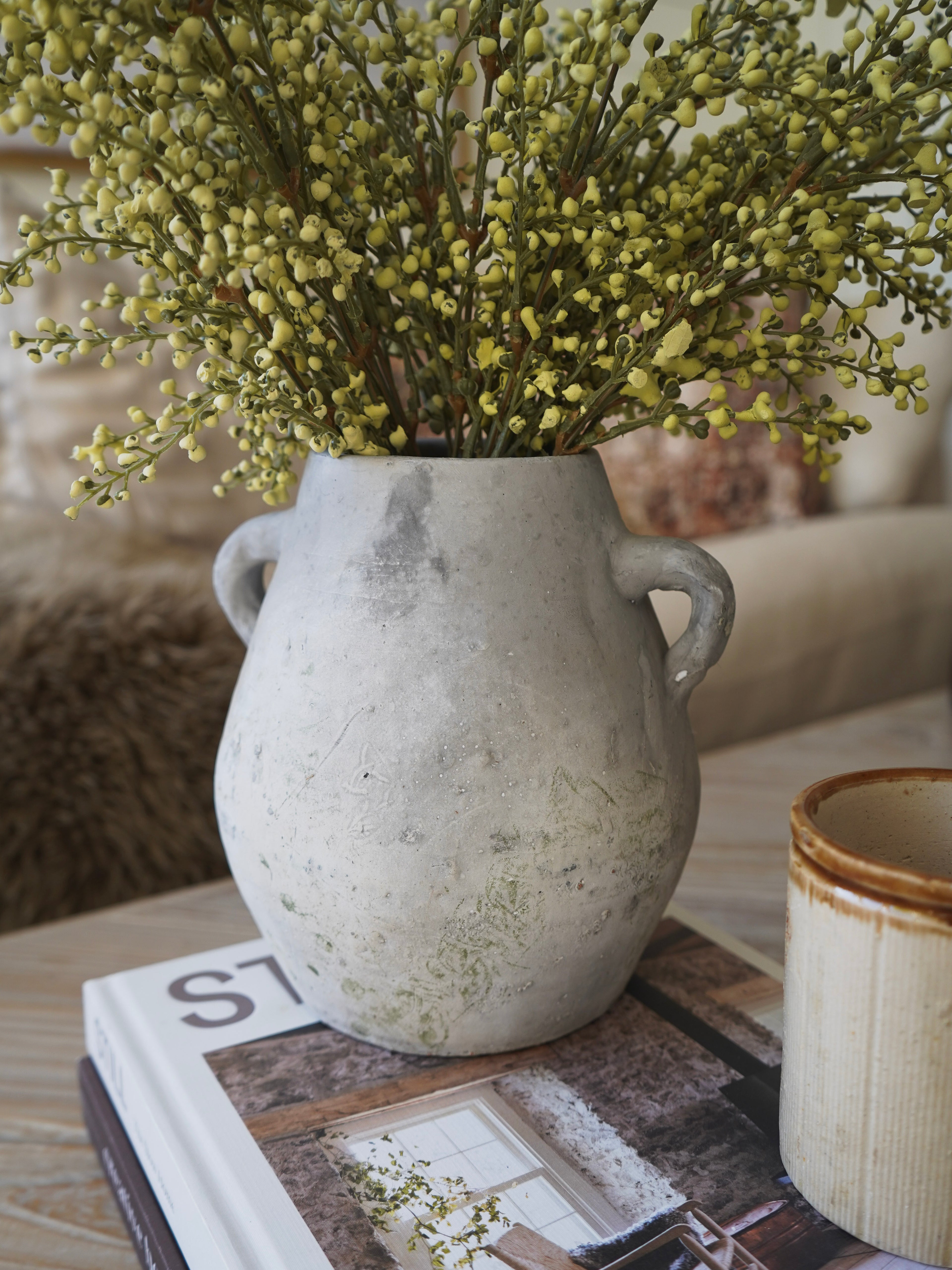 Decorative vase with greenery on a table with books and a cup.