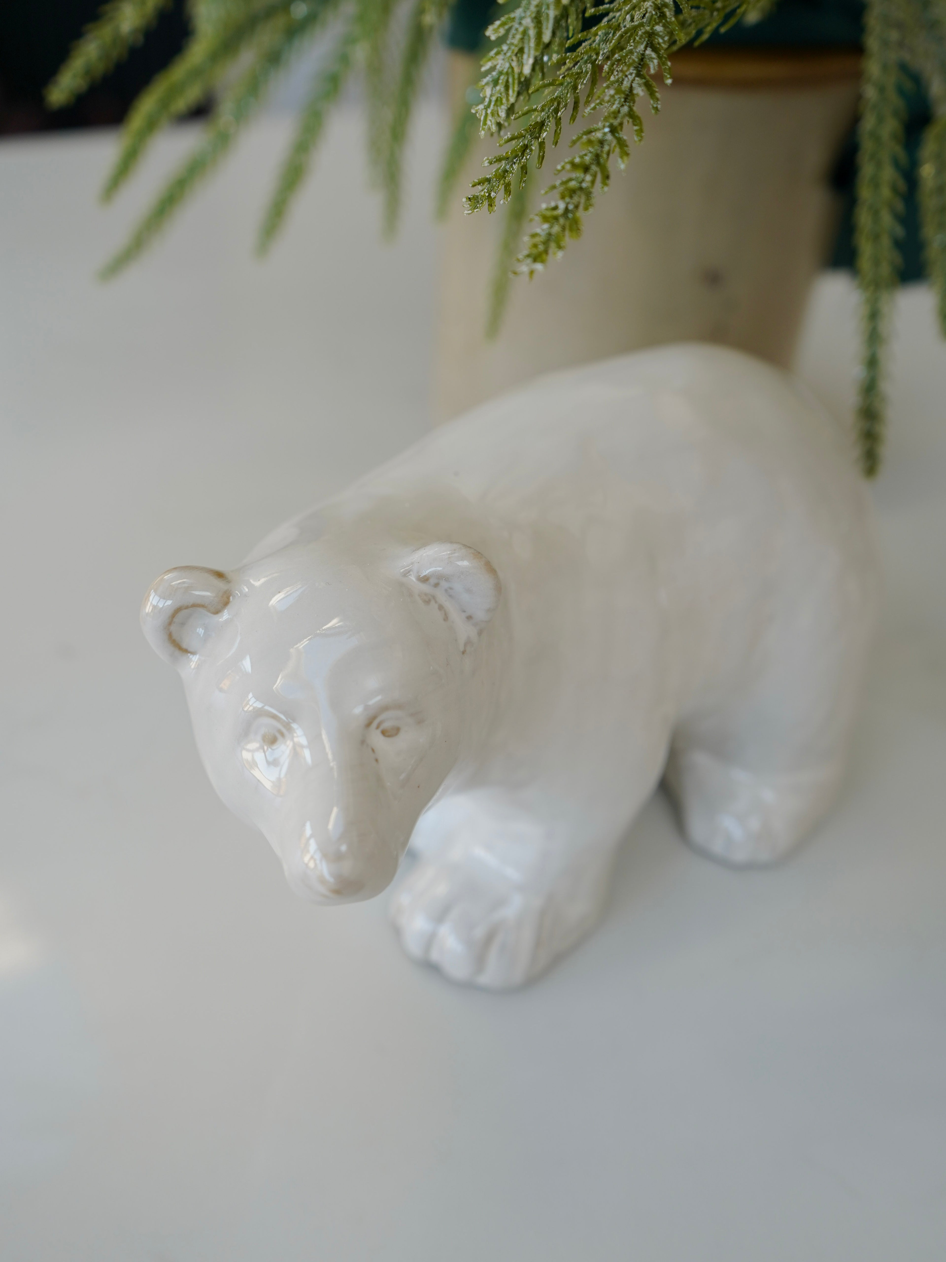 White ceramic bear figurine on a light surface with greenery in the background