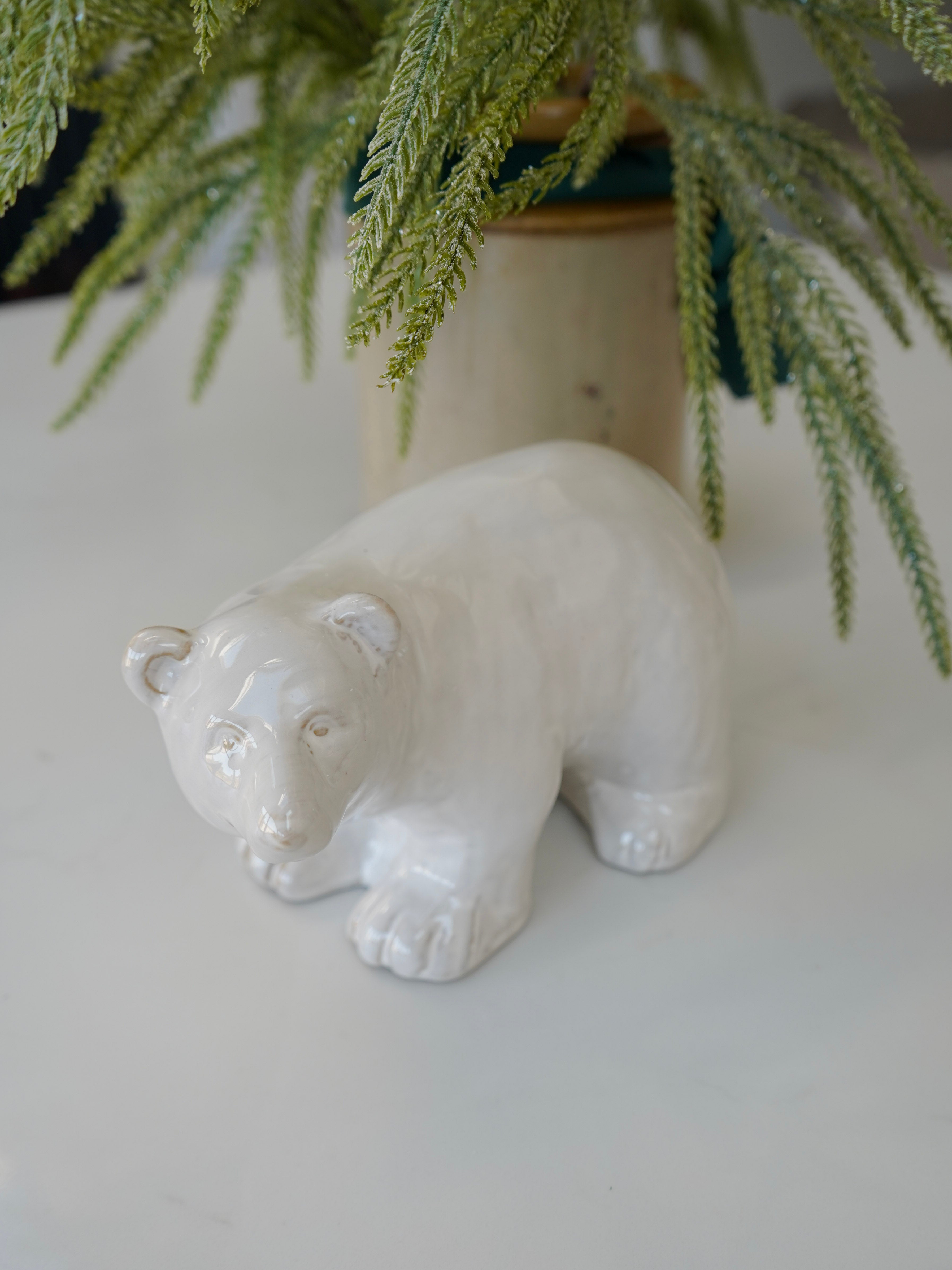 White ceramic bear figurine on a light surface with greenery in the background
