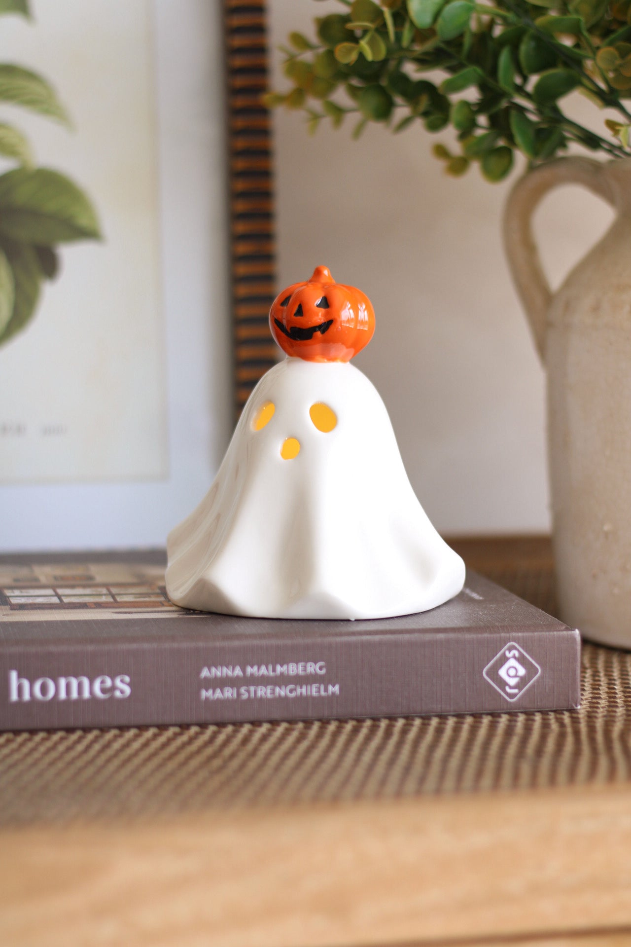Ghost-shaped decorative item with a pumpkin on top, placed on a book