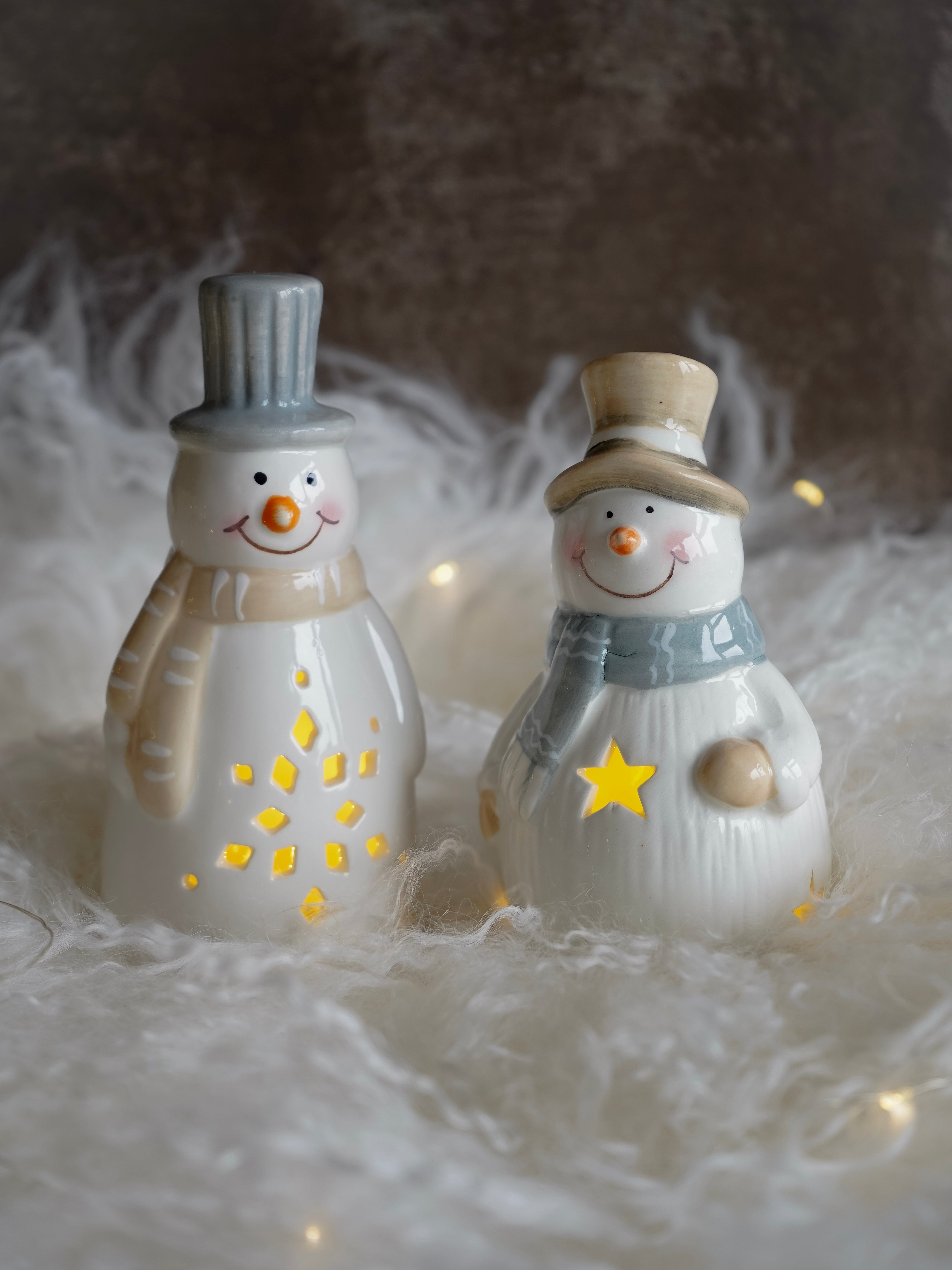 Two decorative snowmen with top hats and scarves on a soft, textured surface.