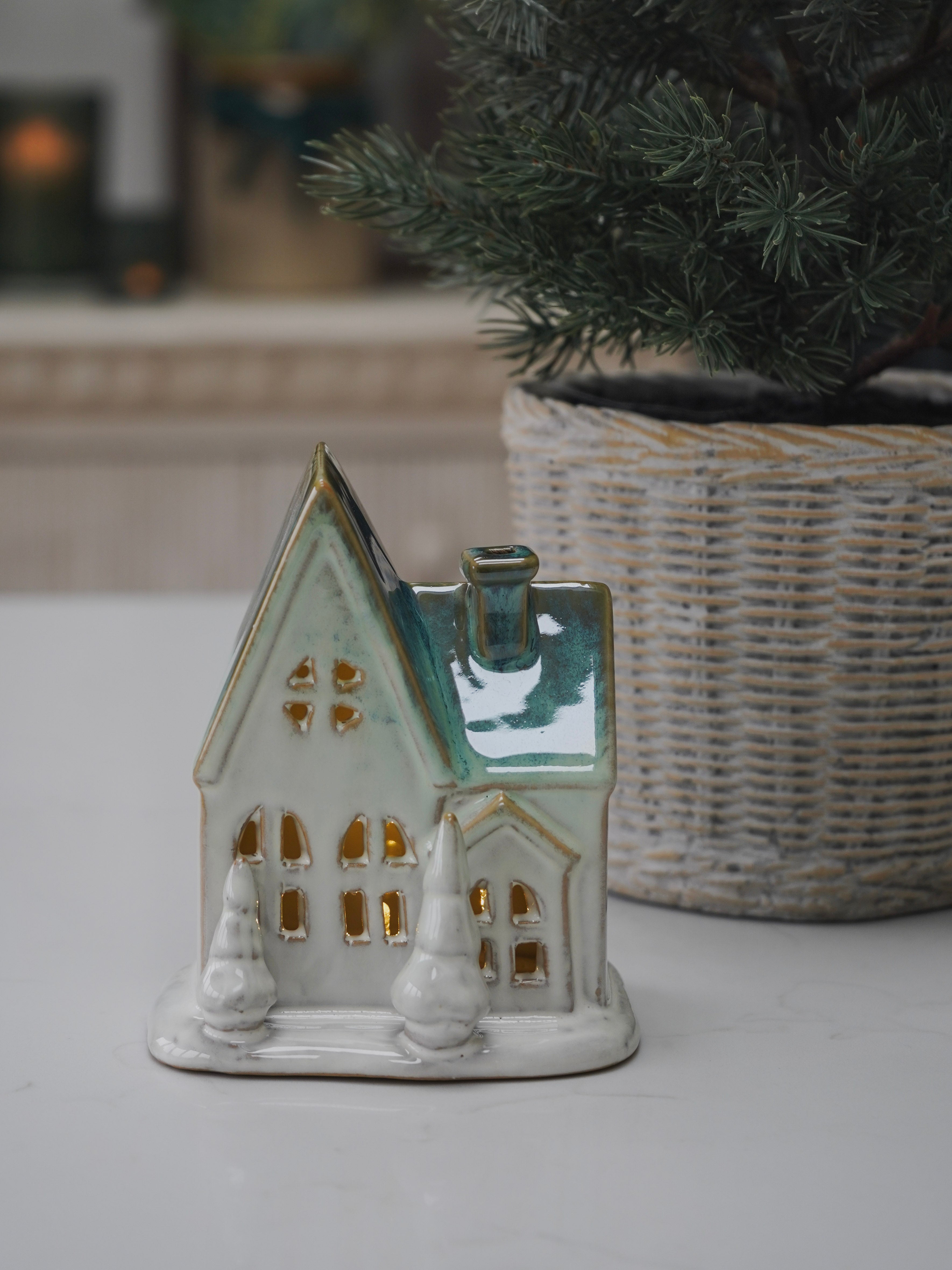 Ceramic house-shaped lantern with decorative elements on a white surface.