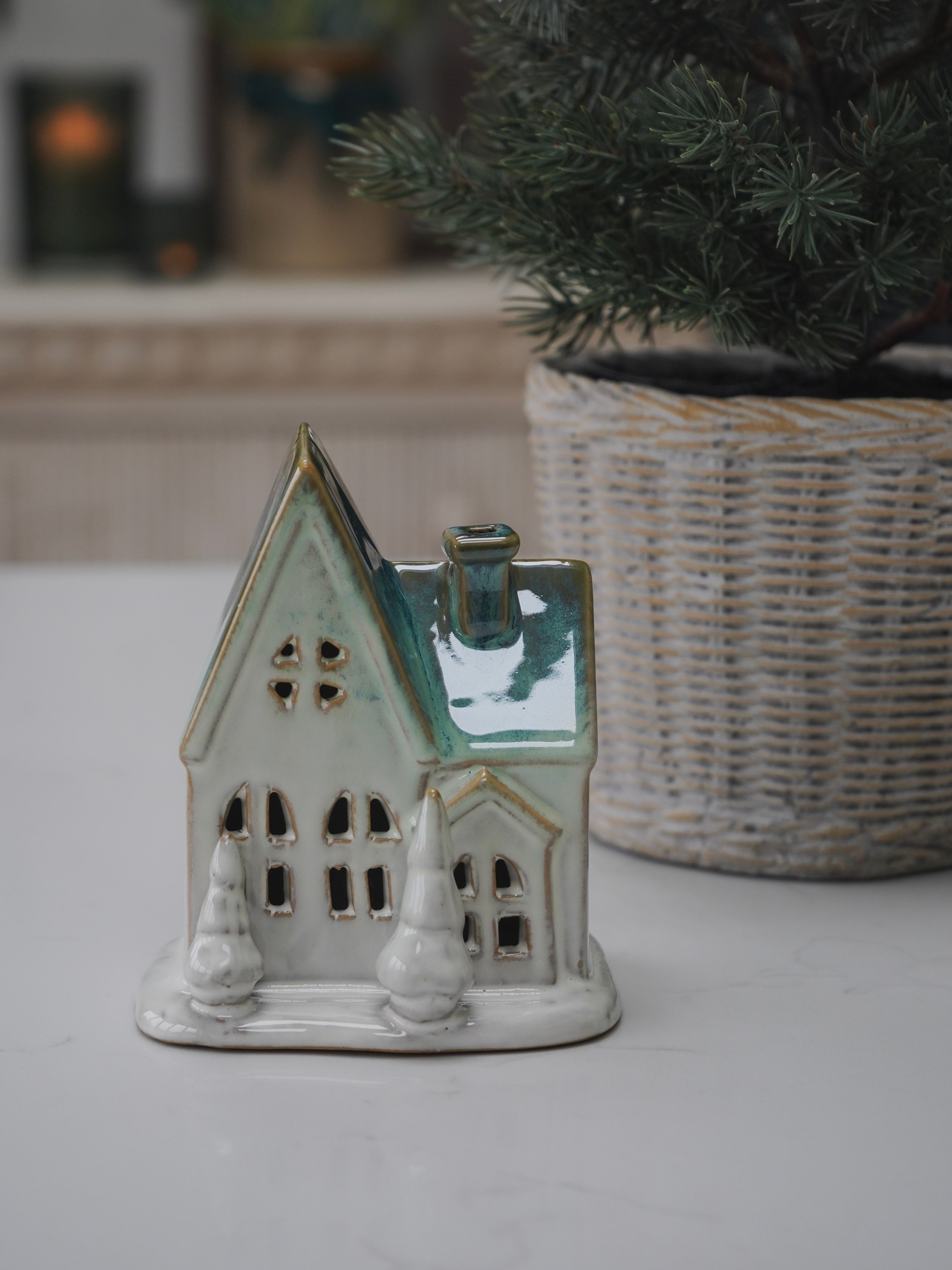 Ceramic house-shaped candle holder on a white surface with a blurred background