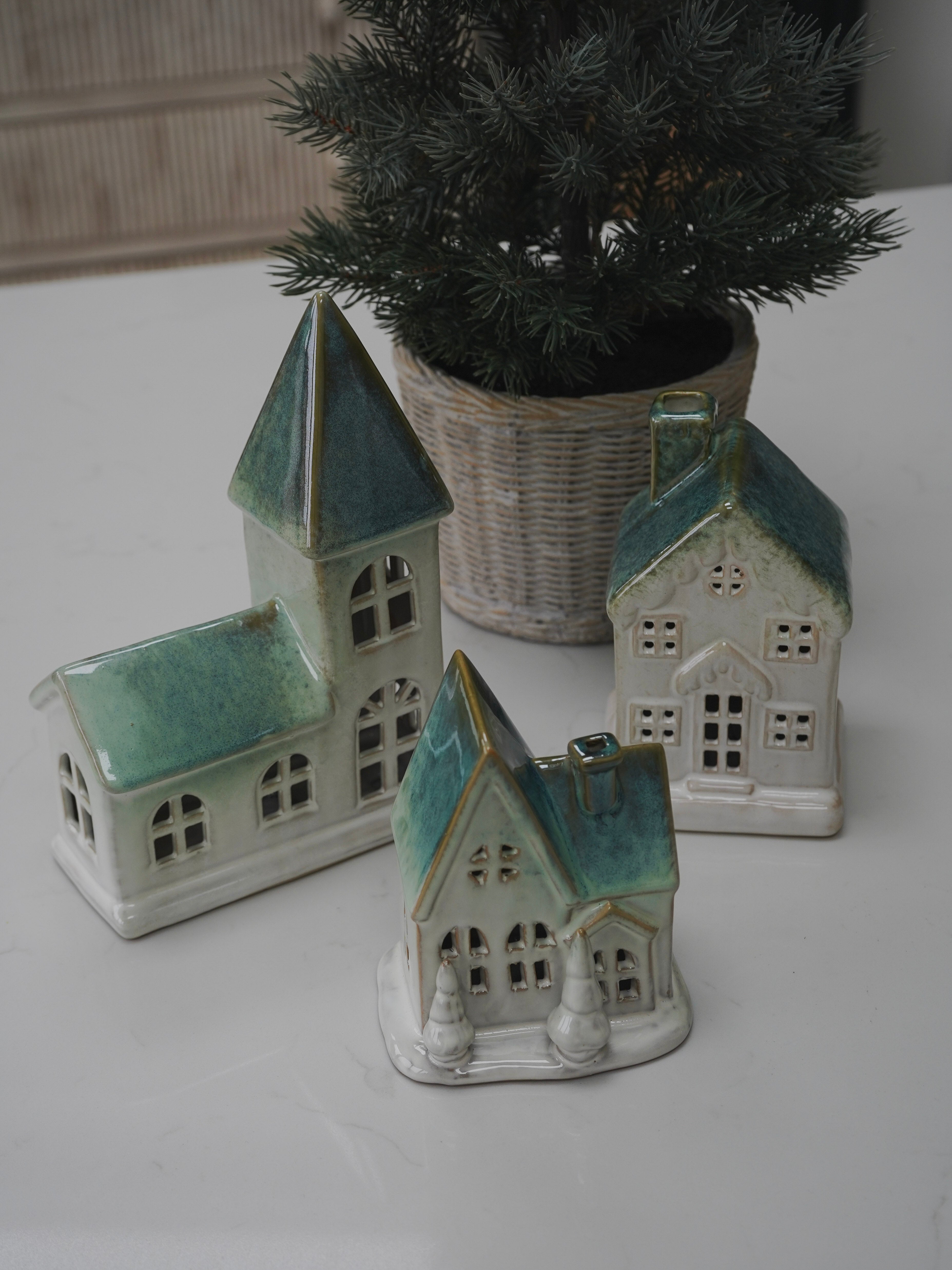 Set of ceramic house-shaped vases with green roofs on a white surface.