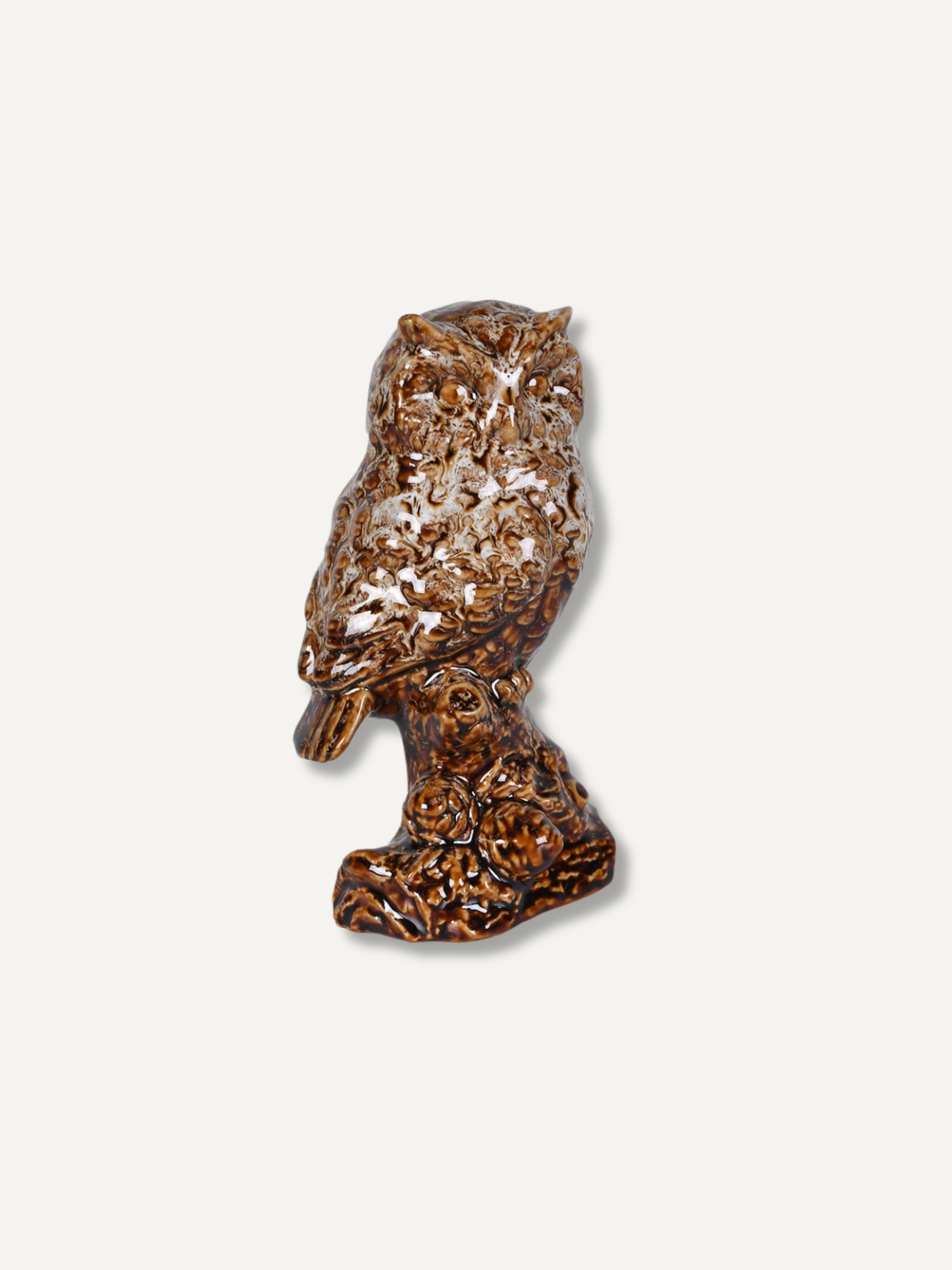 A small owl figurine in a glossy brown and amber marbled pattern, standing on a textured branch base against a light gray background.