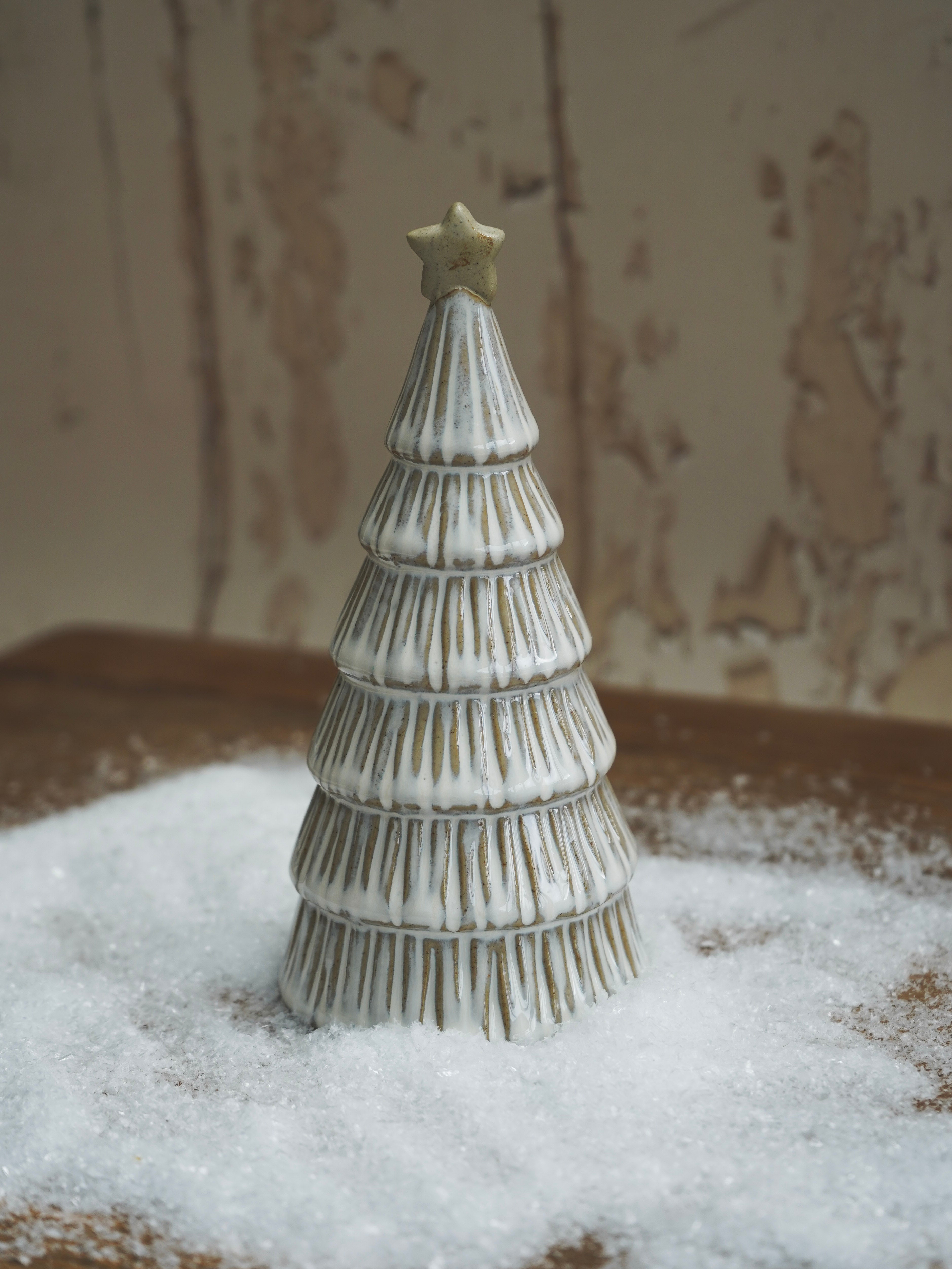 Decorative ceramic Christmas tree with a star on top, placed on a surface with a textured background.