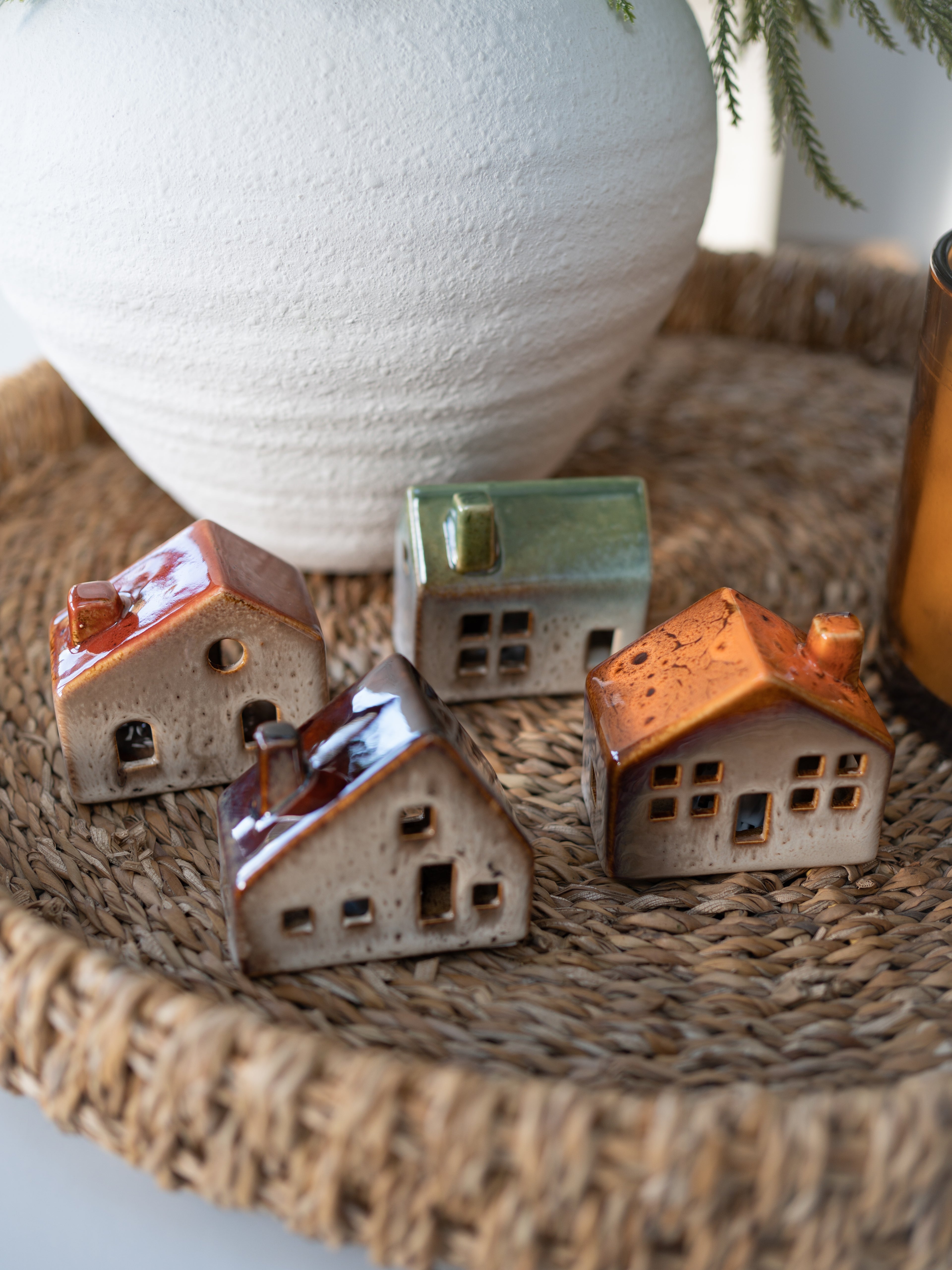 Small ceramic houses on a woven surface with a large white vase in the background