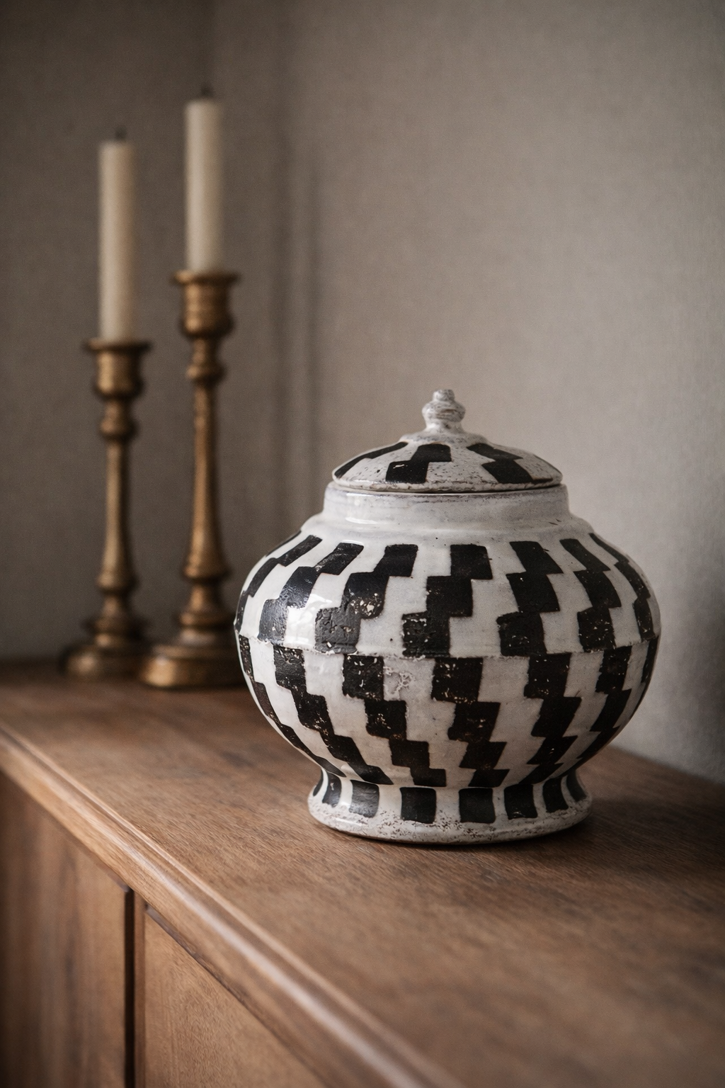 Black and white checkered jar on a wooden surface with two gold candlesticks in the background. Perfect for home styling and accessorising