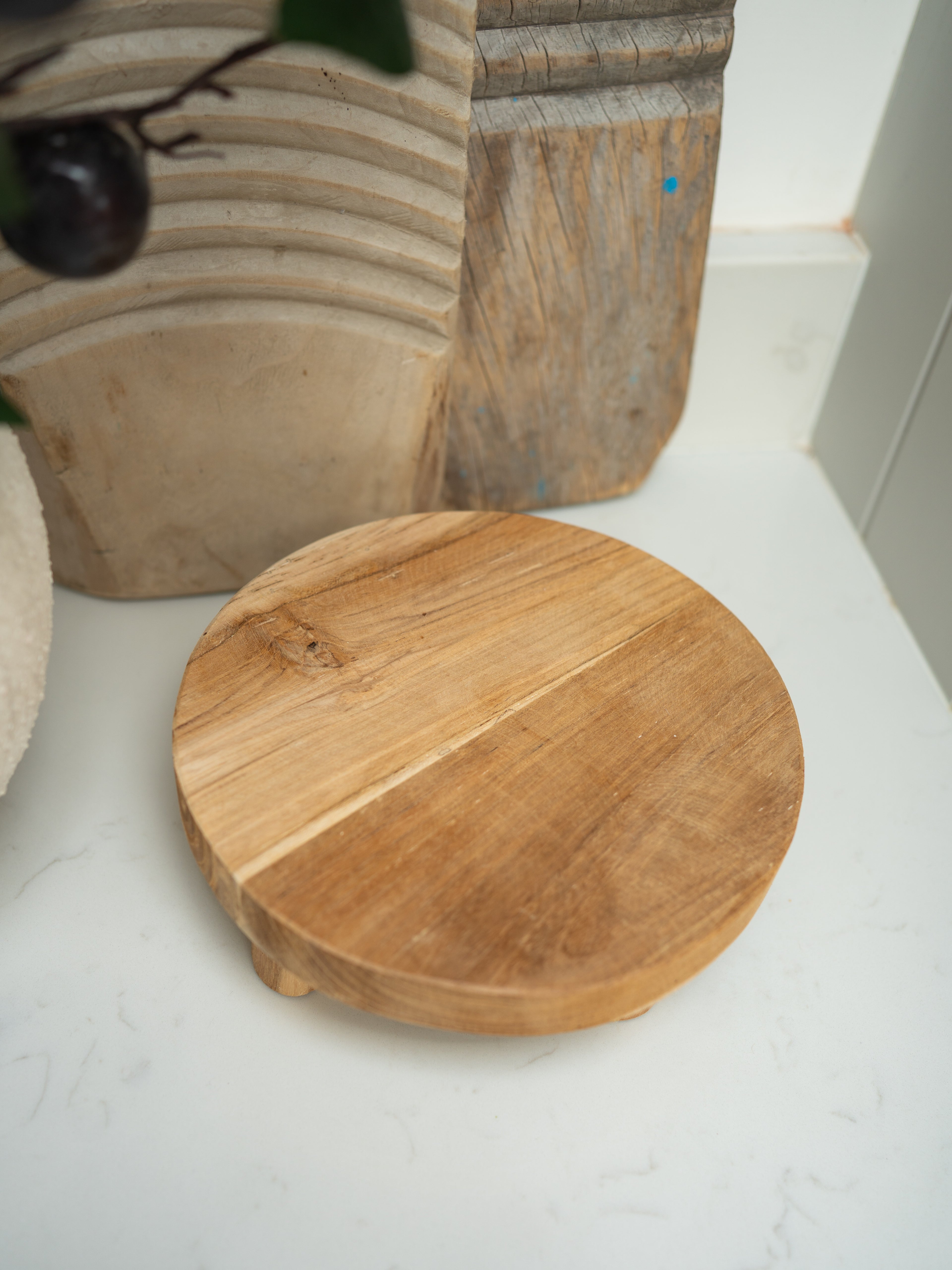 Wooden round display stand on a light surface with decorative elements in the background
