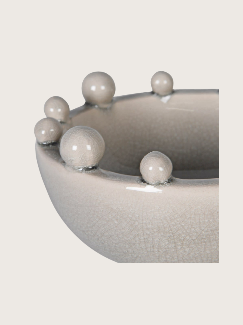 Cream ceramic bowl with bobble decorative elements on a light gray background