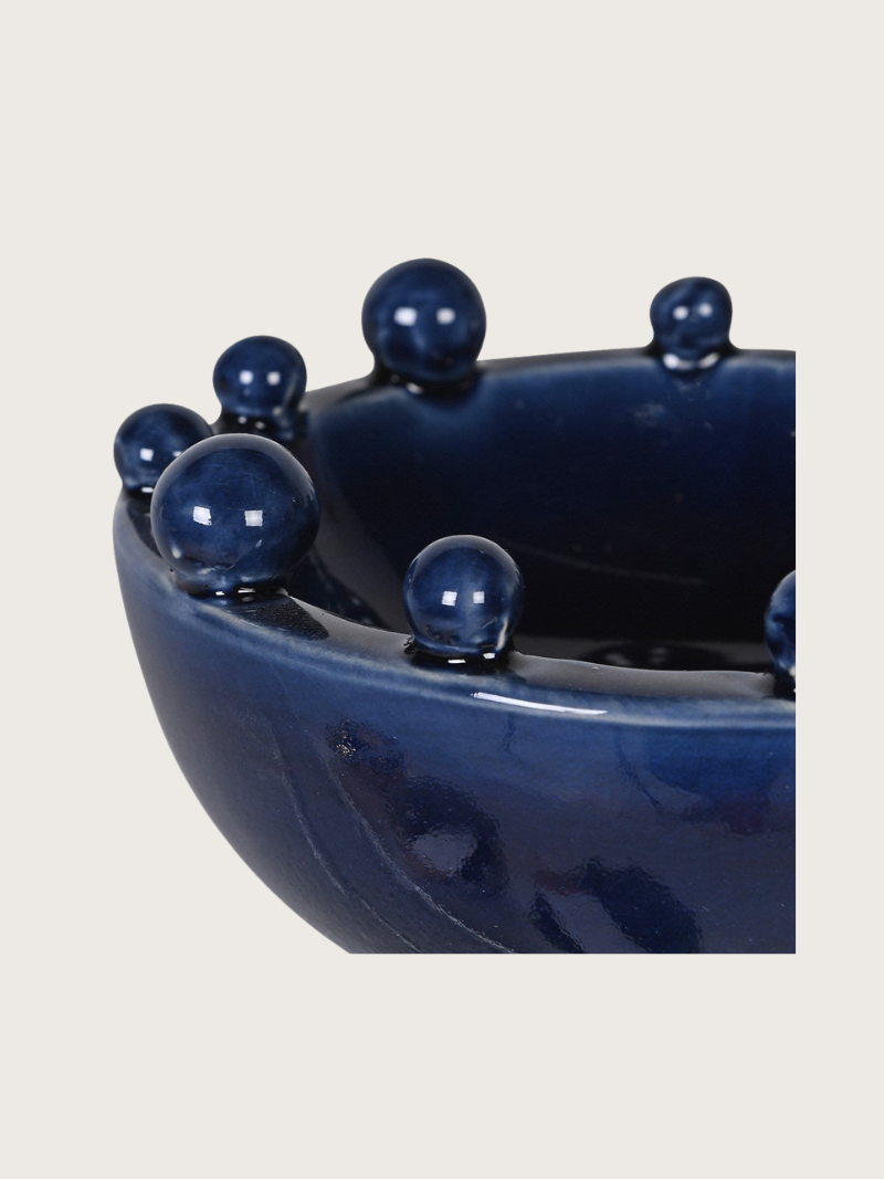 Blue ceramic bowl with bobble decorations on a light gray background