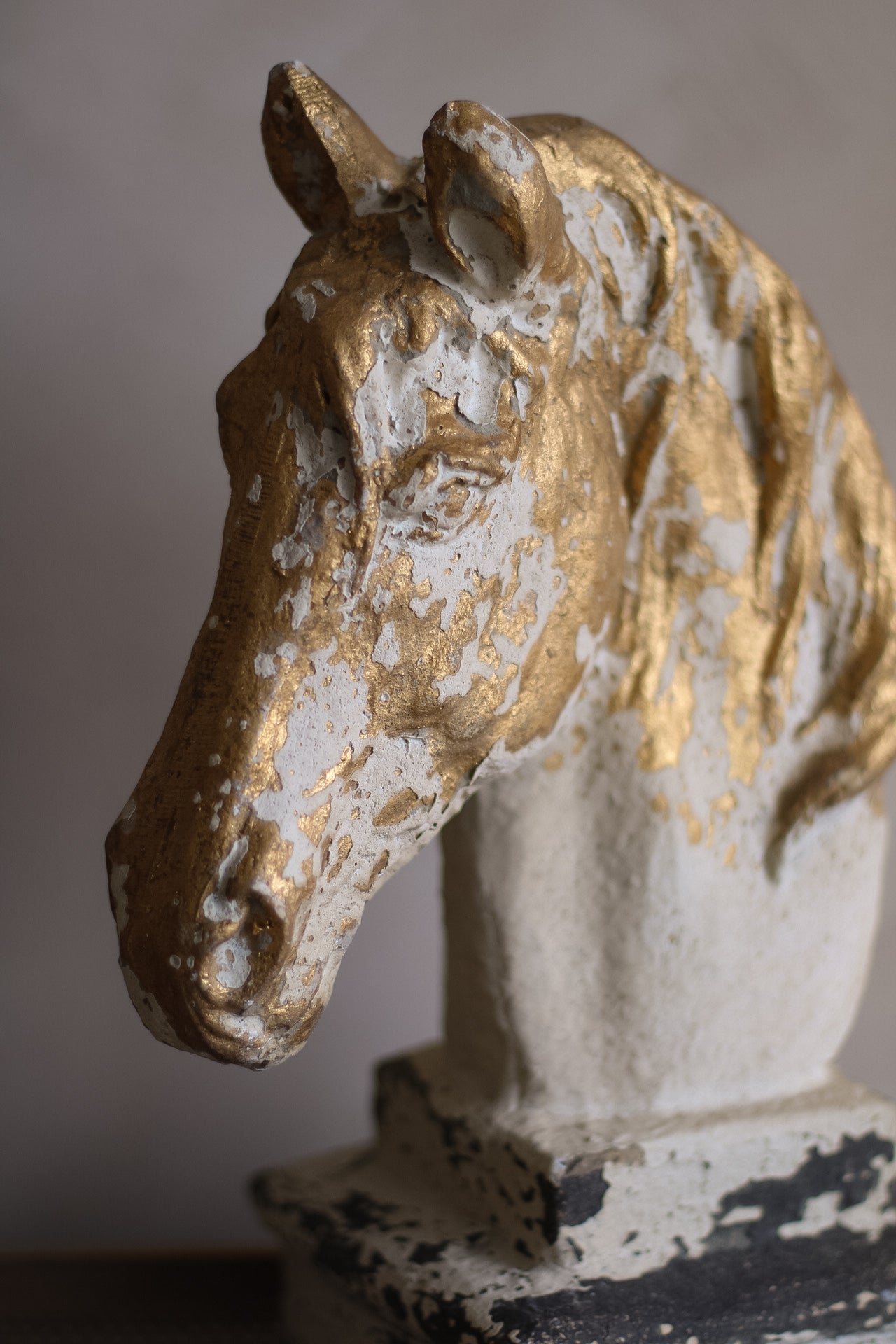 Decorative horse head sculpture with gold and white finish on a plain background