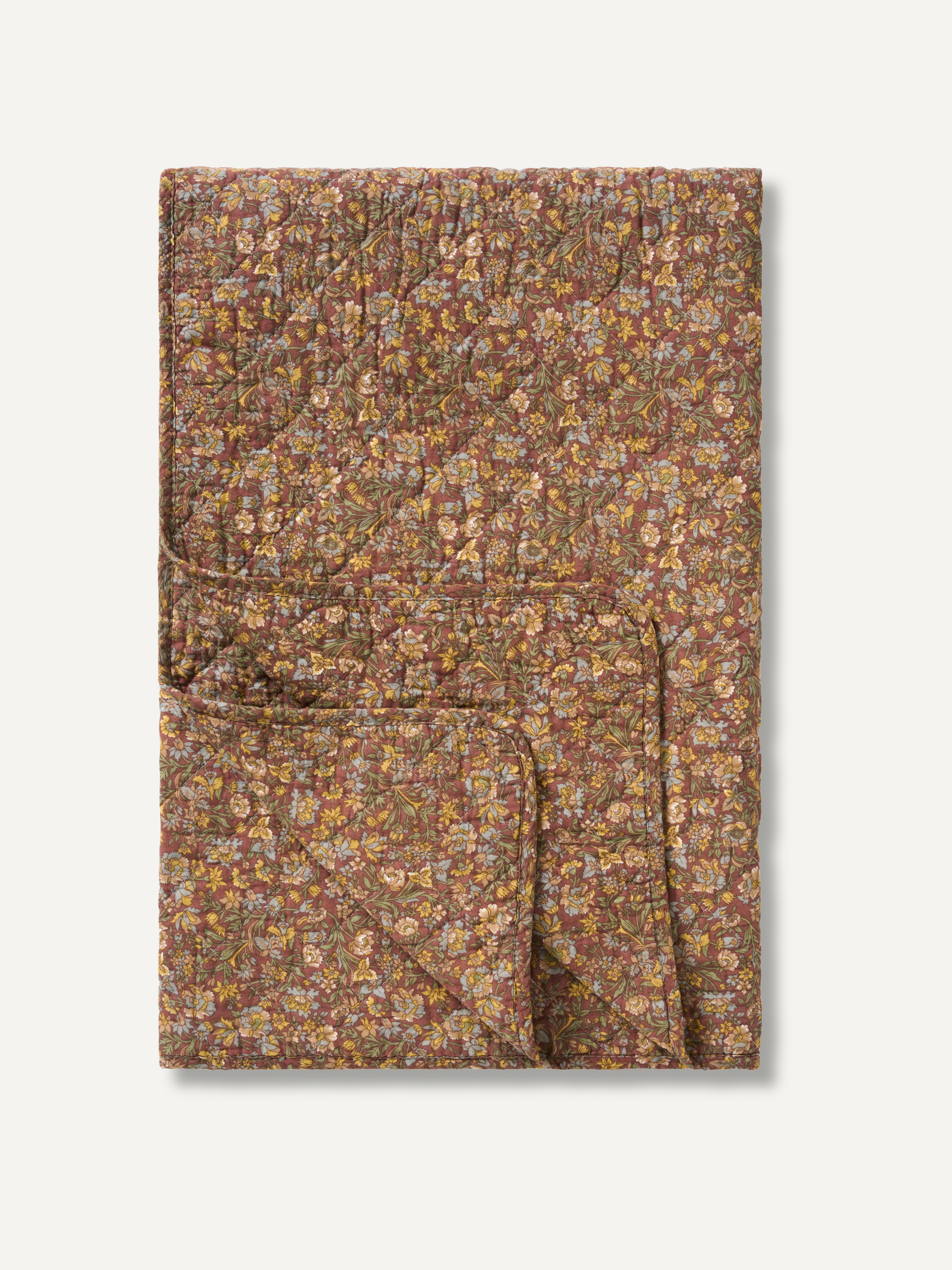 A folded quilted blanket with a dense floral and geometric pattern in earthy brown, beige, and muted orange tones, presented on a clean off-white background.