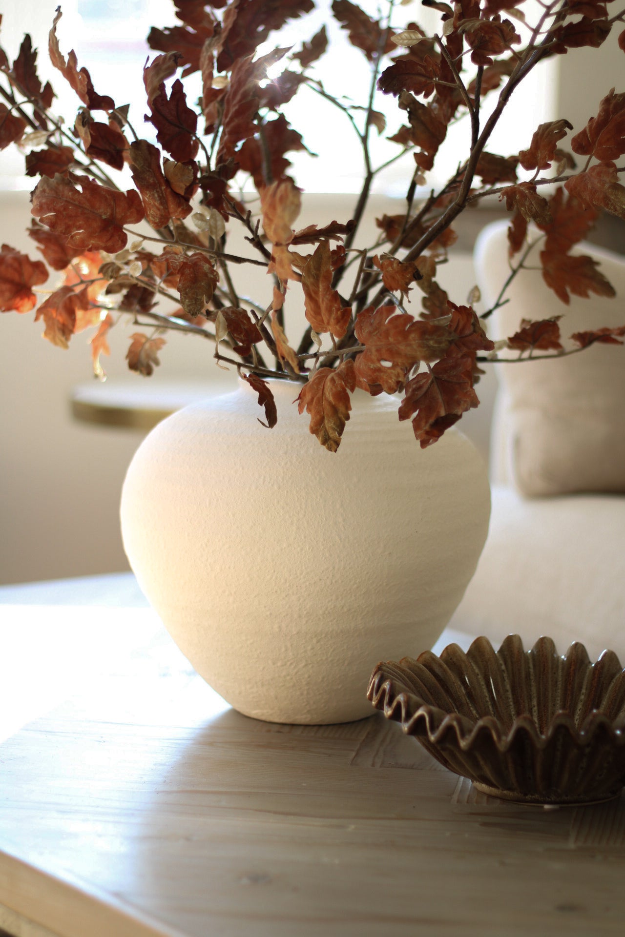 White vase with dried leaves on a wooden surface