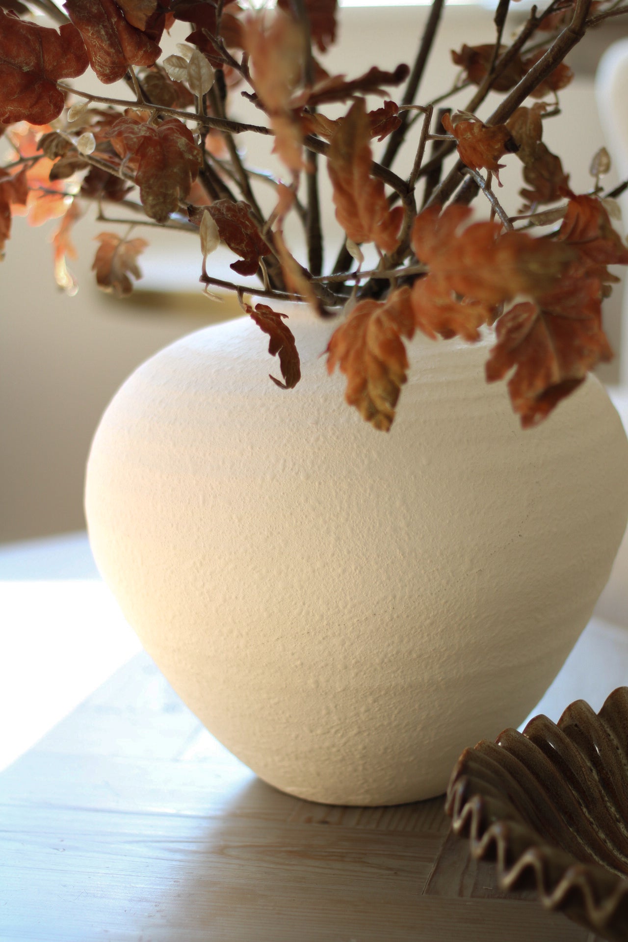 White ceramic vase with dried leaves on a wooden surface
