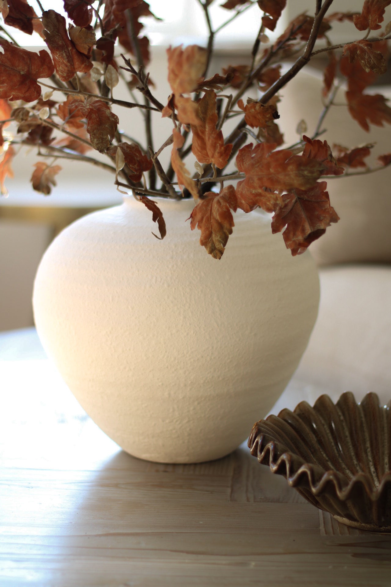 White vase with dried leaves on a wooden surface