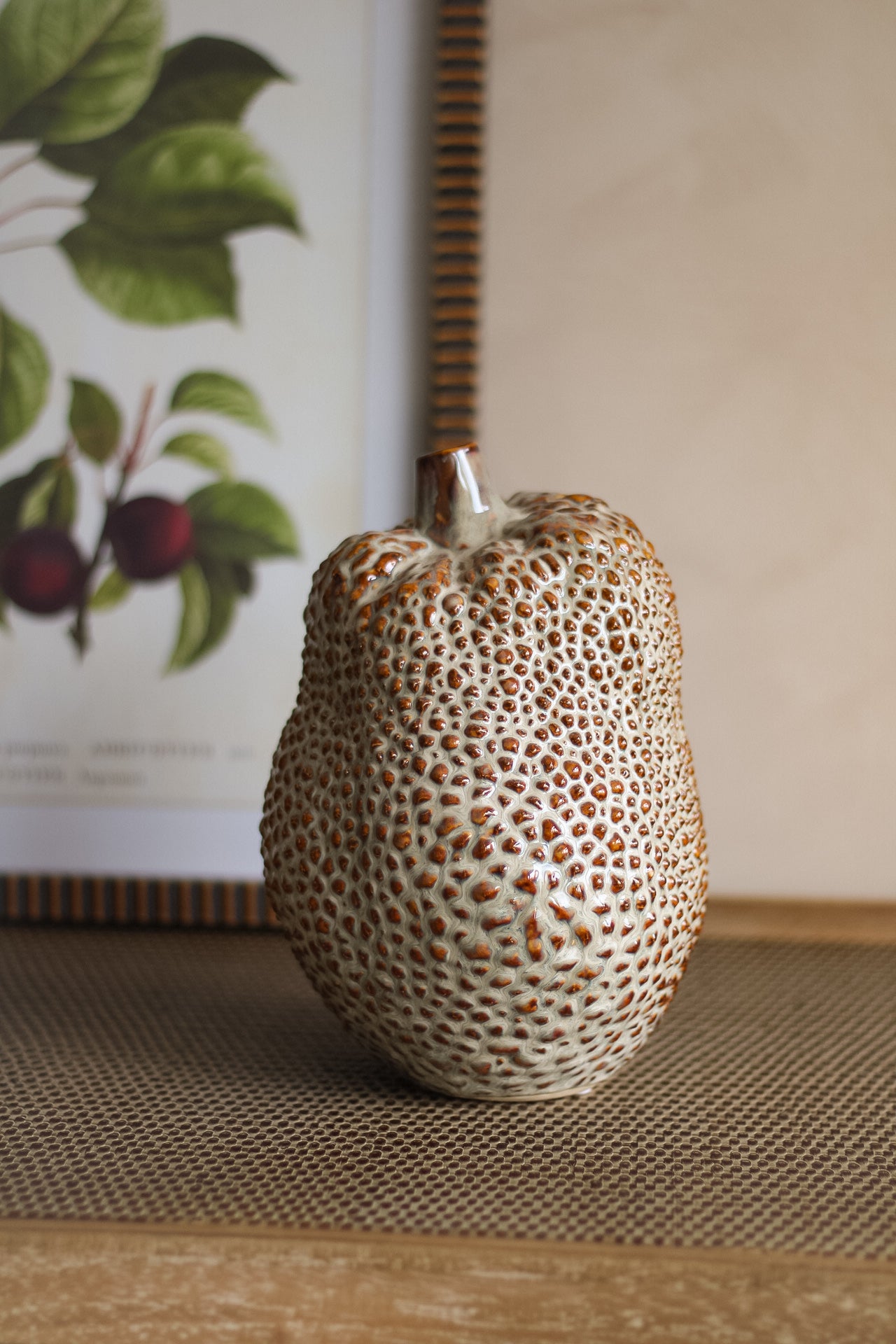 Decorative ceramic durian vase with textured surface on a textured surface with a framed picture in the background.