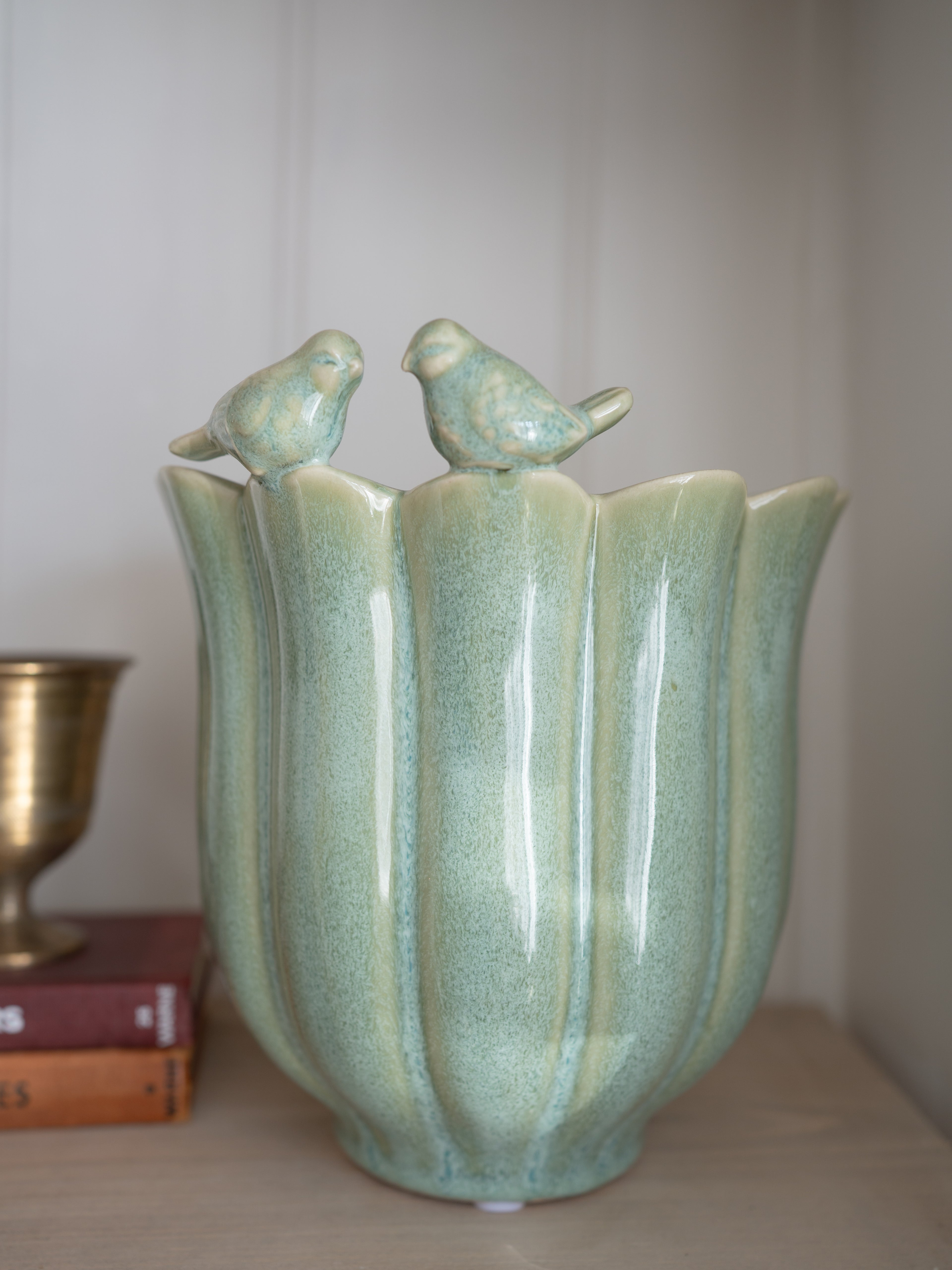 Green ceramic plant pot with bird designs on a neutral background