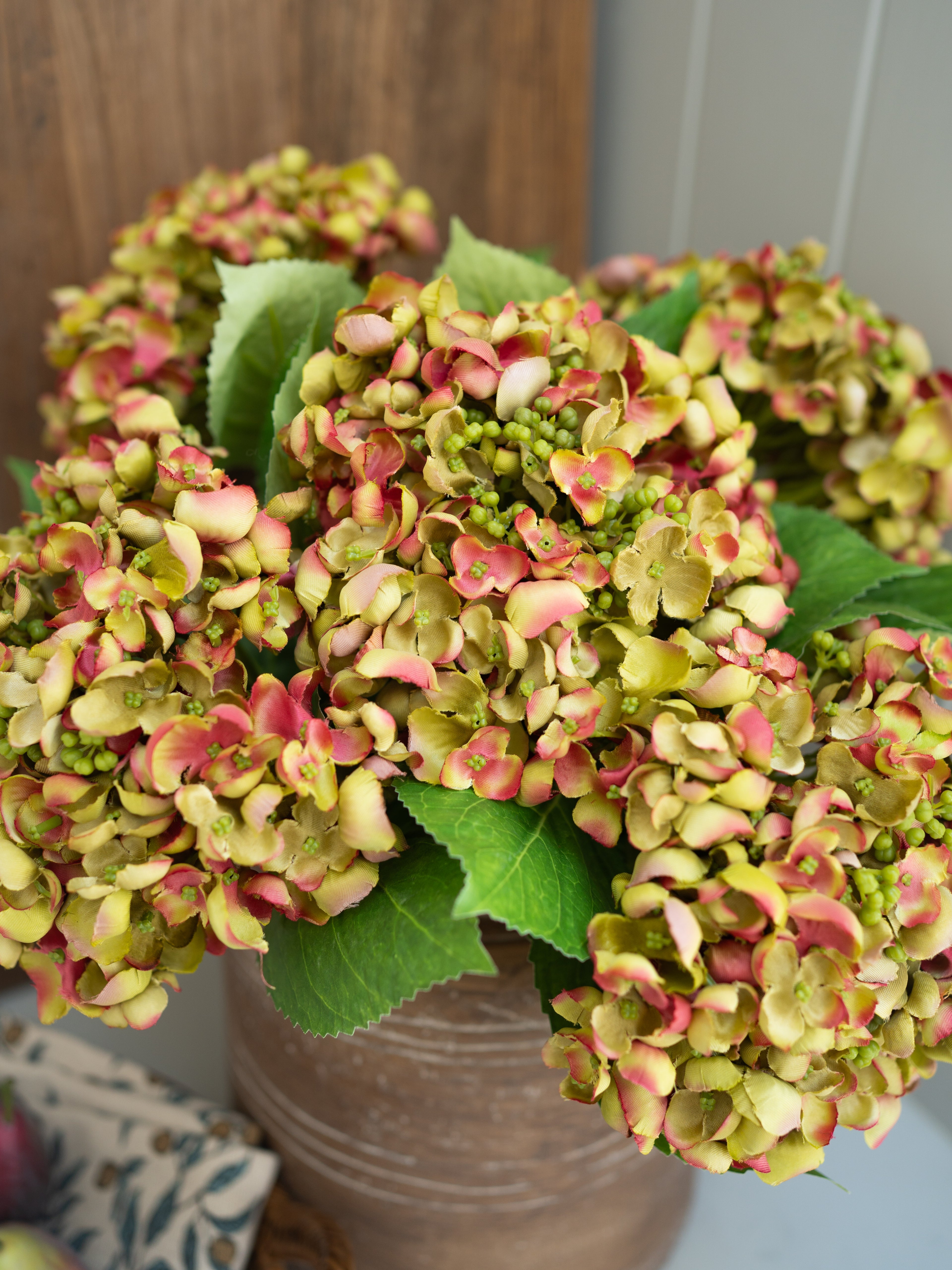 Bouquet of pink and green artificial hydrangea flowers in a vase on a wooden surface.